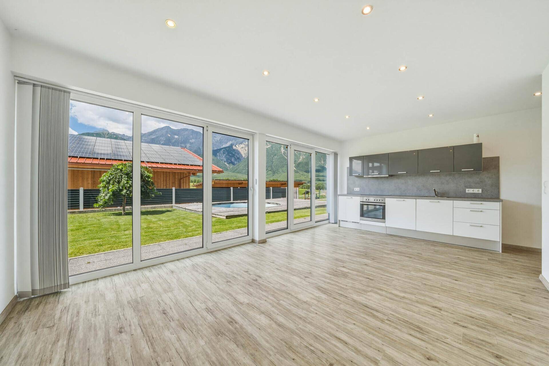 Heller offener Wohnbereich mit integrierter Küche, großen Fenstern und direktem Blick auf den Garten und die Berge.