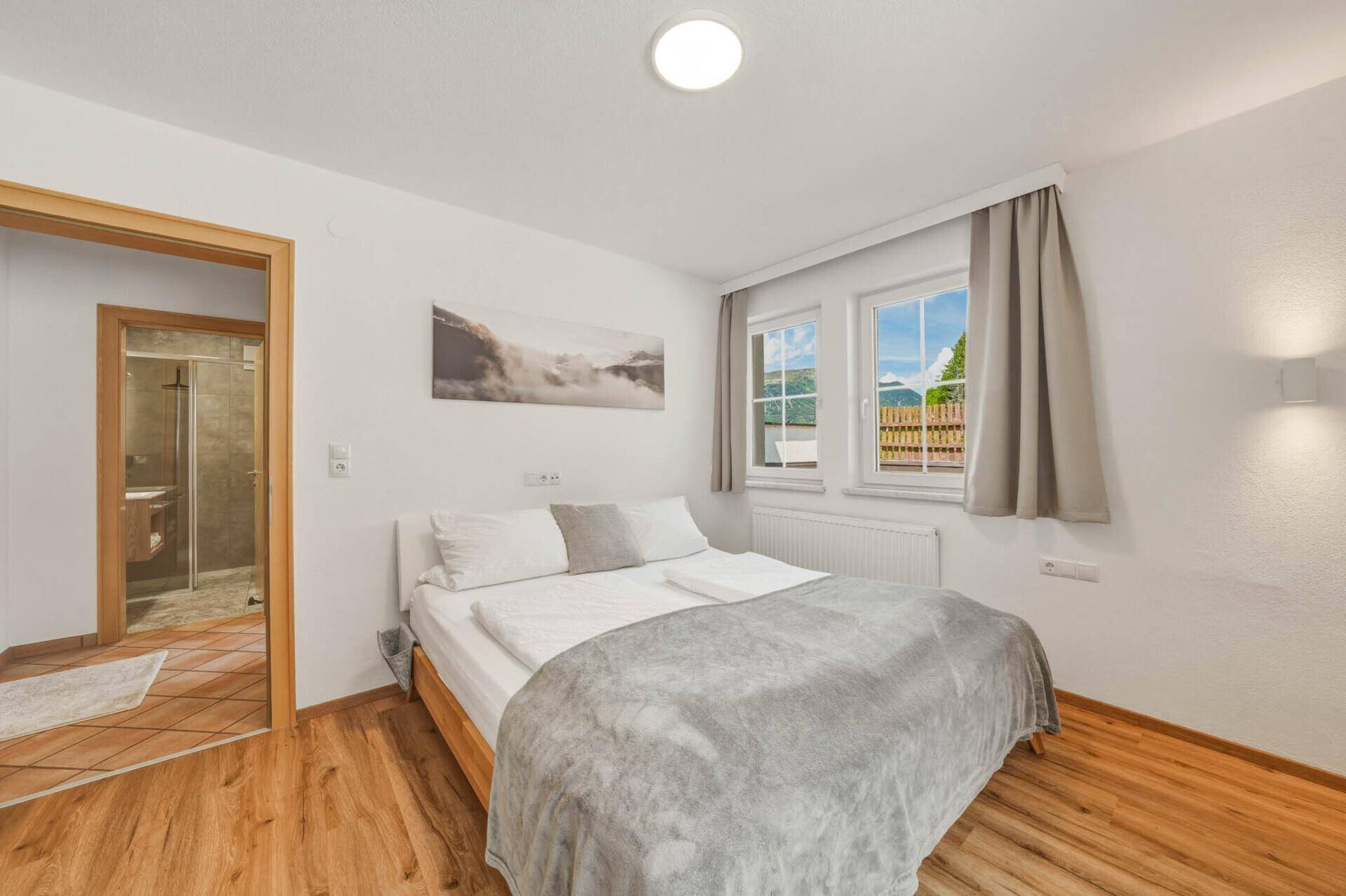 Helles Schlafzimmer mit Holzboden, bequemen Bett und direktem Zugang zu einem modernen Badezimmer.
