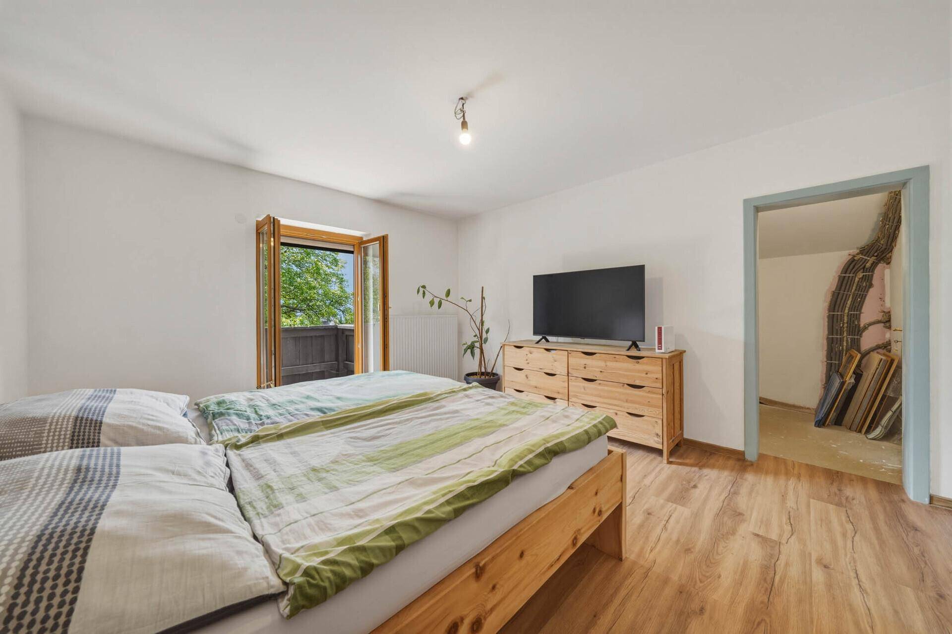 Schlafzimmer mit Holzbett, Kommode und Zugang zu einem Balkon sowie einem weiteren Raum.