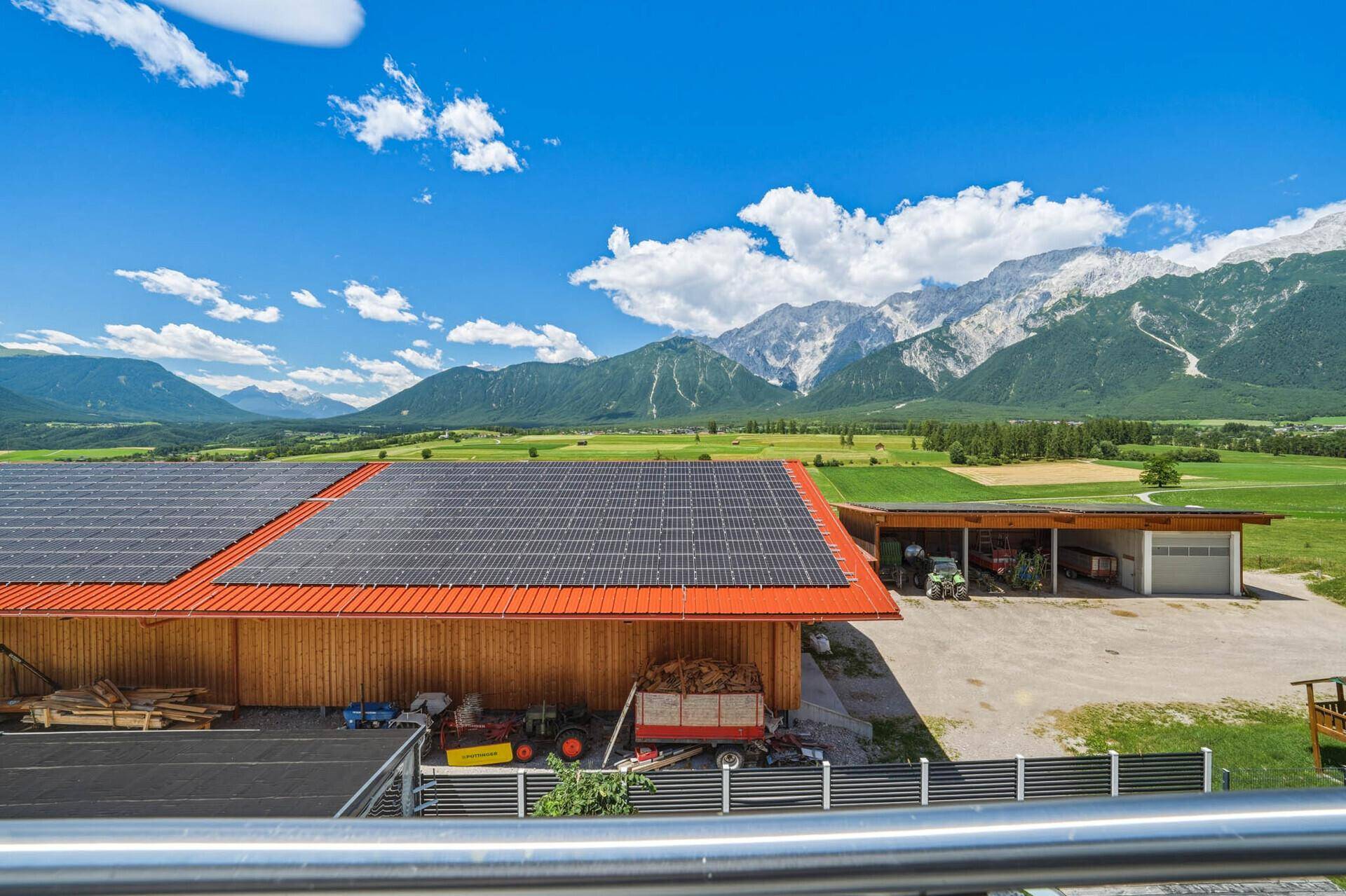 Weitläufiger Ausblick auf die Bergkette, Felder und landwirtschaftliche Gebäude mit Solaranlagen.
