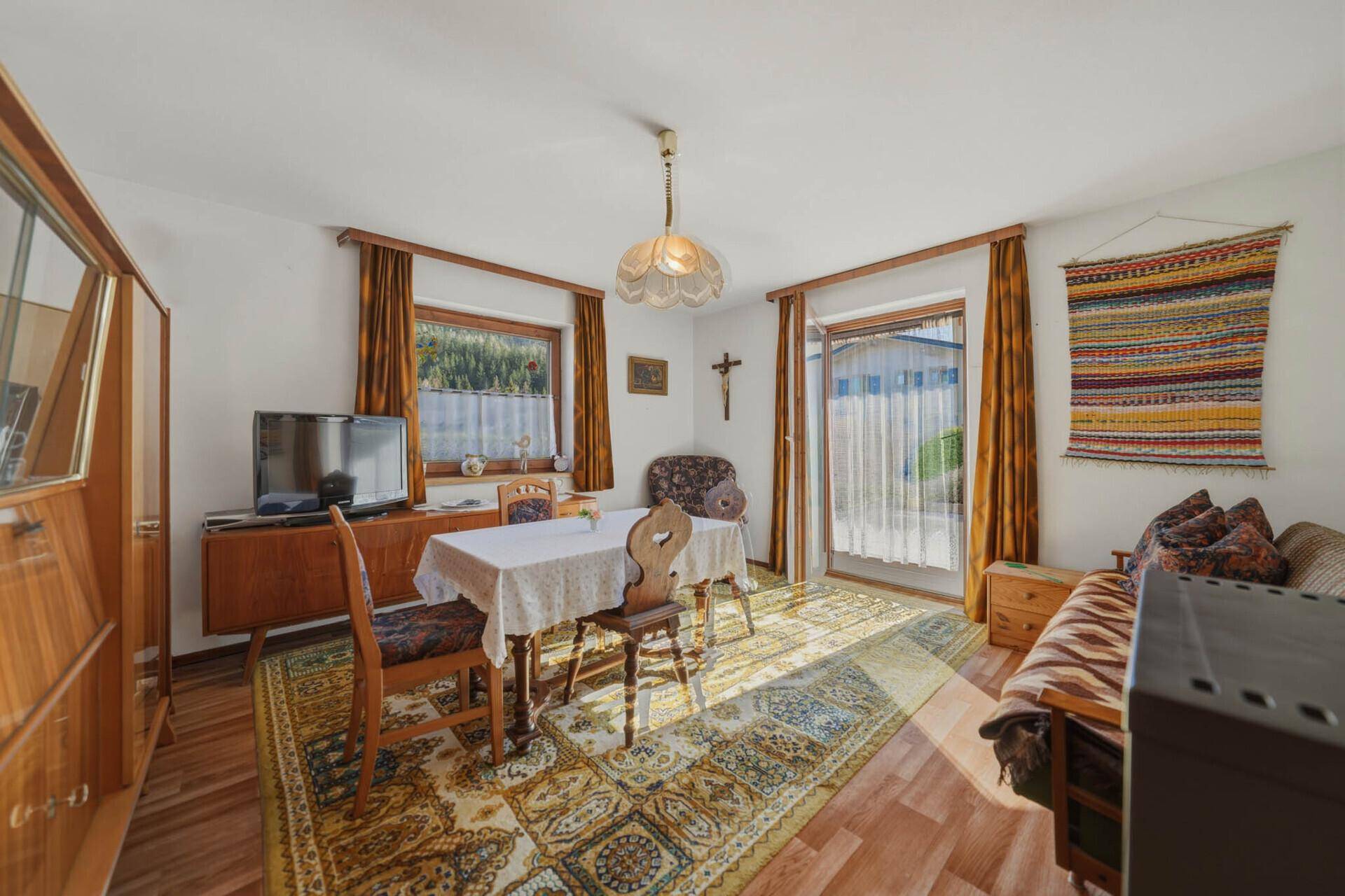 Gemütlicher Wohn-Essbereich mit traditionellen Holzmöbeln, Teppichboden und Zugang zur Terrasse.