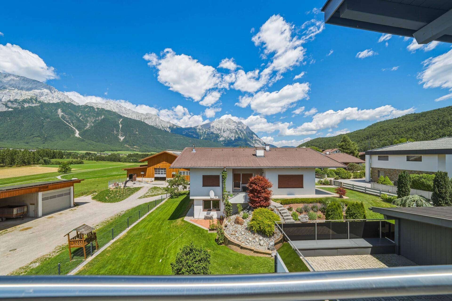 Weitläufiger Blick vom Balkon auf das Anwesen mit Garten, umliegenden Feldern und beeindruckender Bergkulisse.
