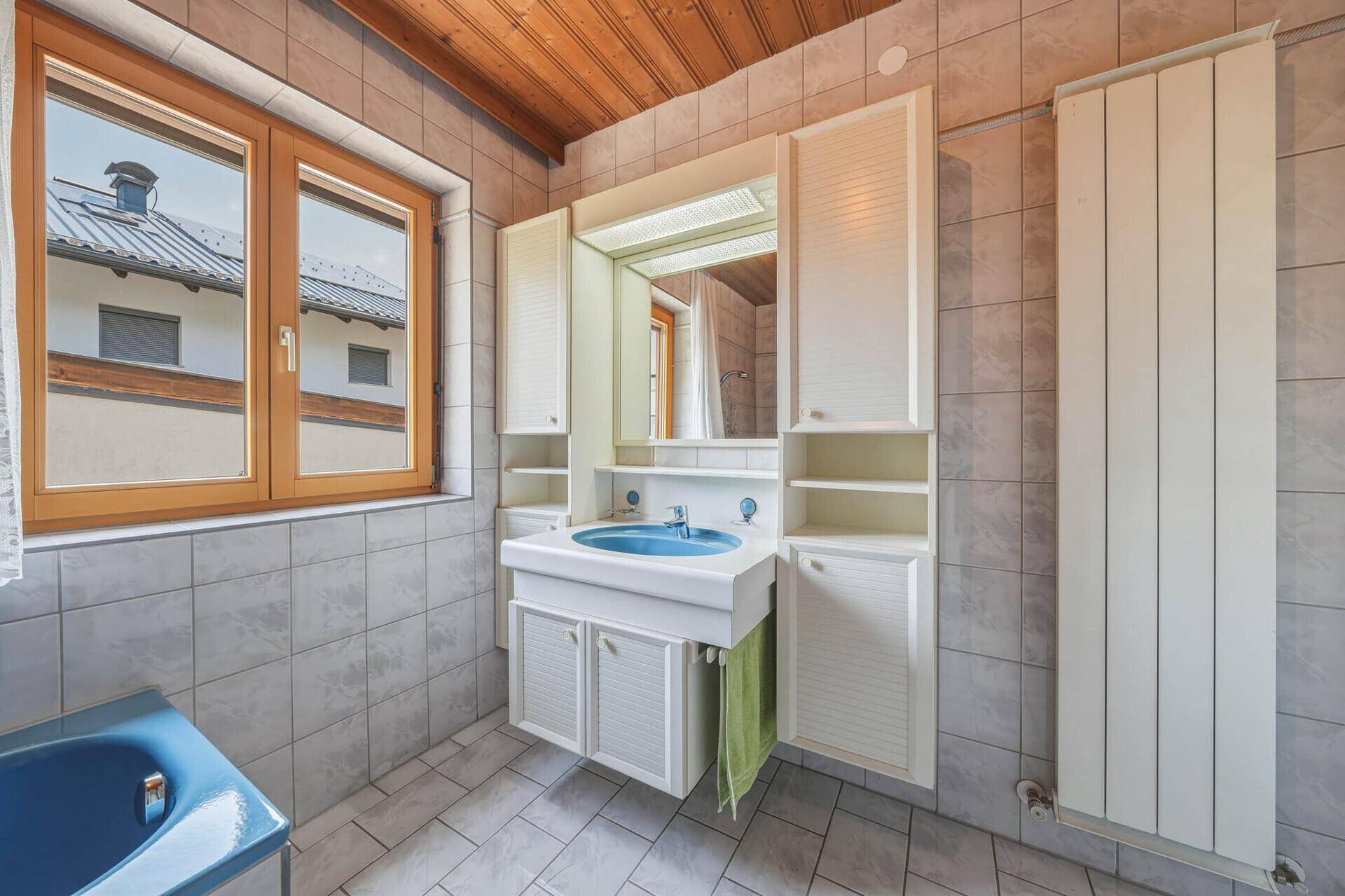 Badezimmer mit Waschtisch, Spiegelschrank, Heizkörper und Fenster mit Blick auf die Nachbarschaft.