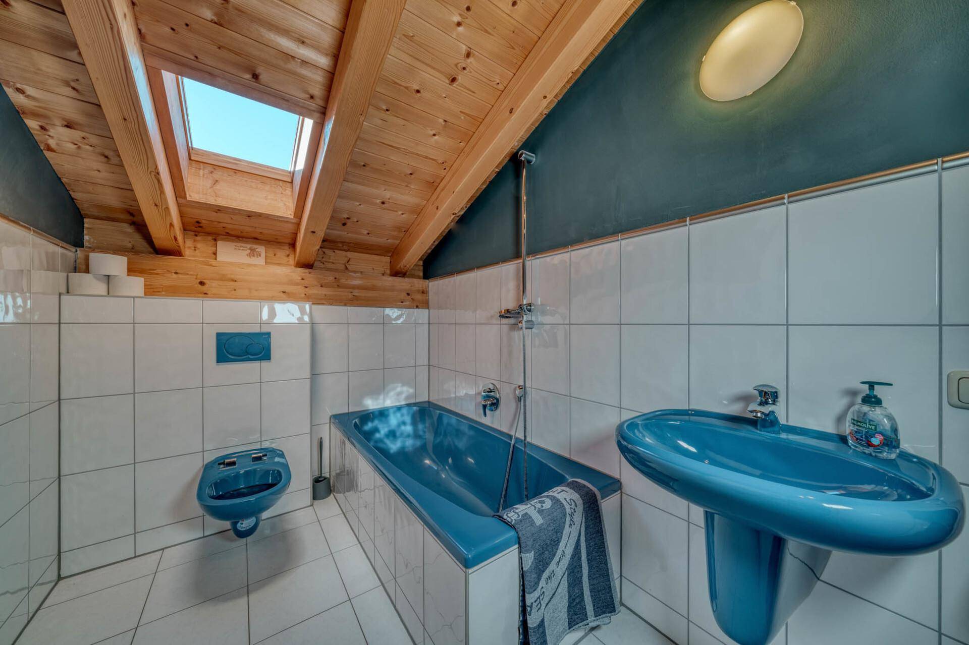 Badezimmer im Dachgeschoss mit blauer Badewanne, Waschbecken und Dachfenster.
