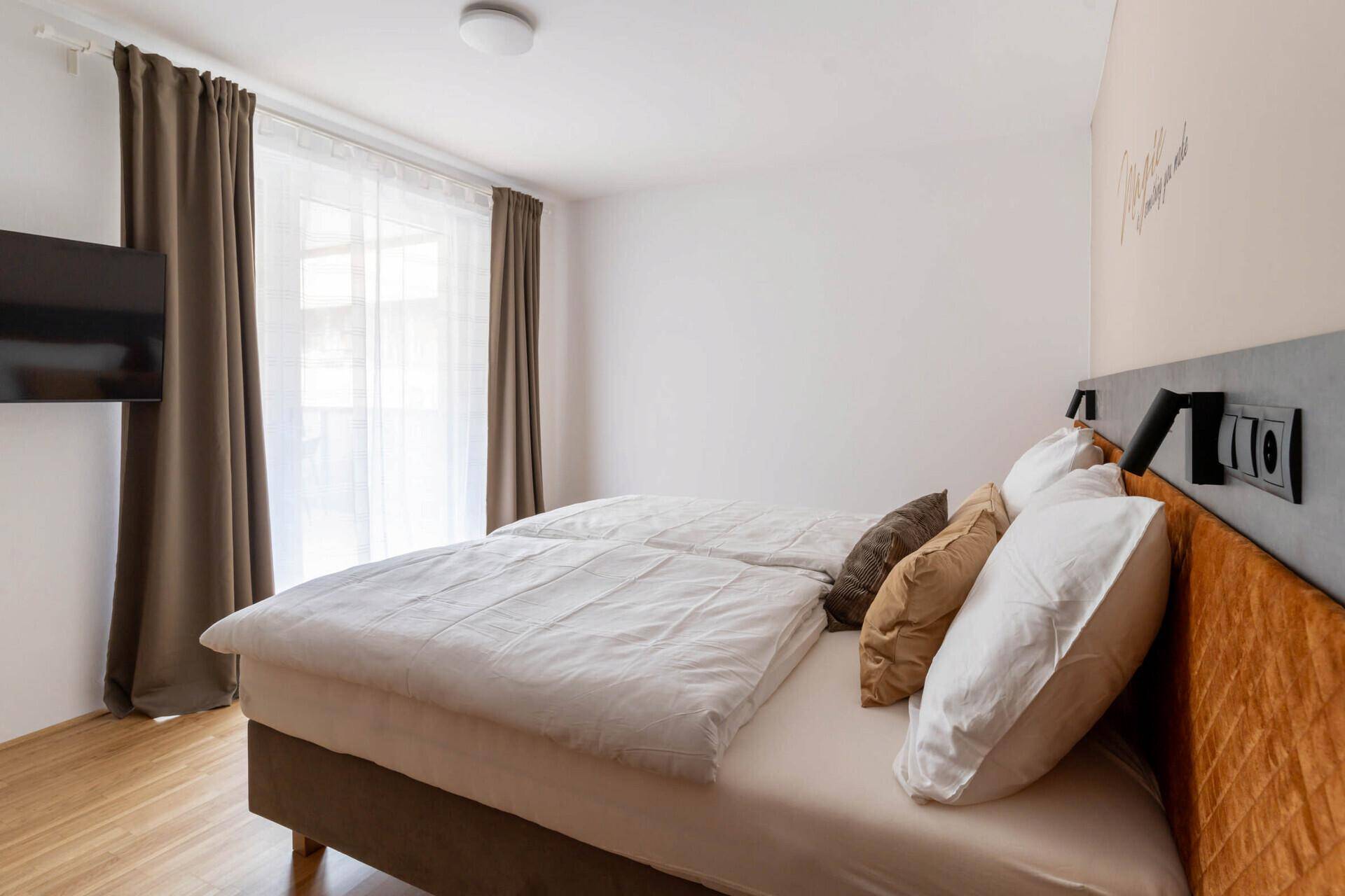 Helles Schlafzimmer mit Doppelbett, Holzboden und Fenster mit Vorhängen.
