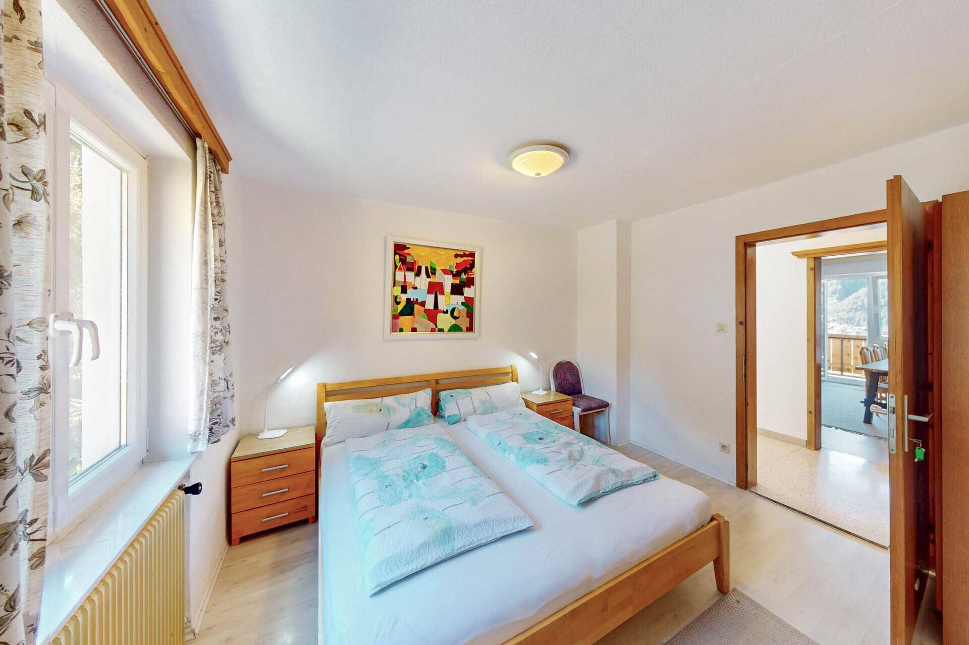Helles Schlafzimmer mit Doppelbett, Teppichboden und Blick auf die Berge.