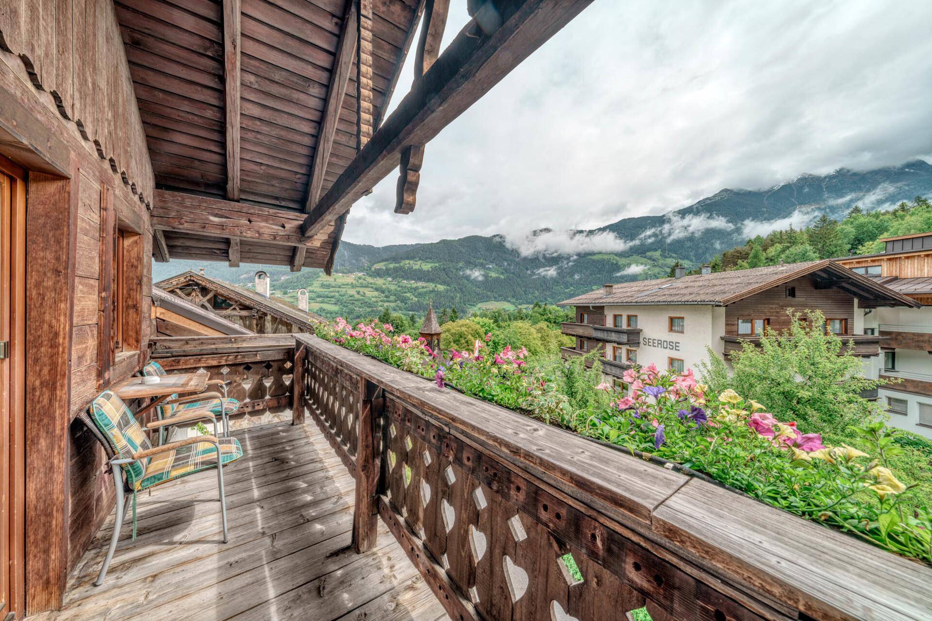 Malerischer Holzbalkon mit bunten Blumenkästen, Sitzgelegenheiten und weitem Bergblick.