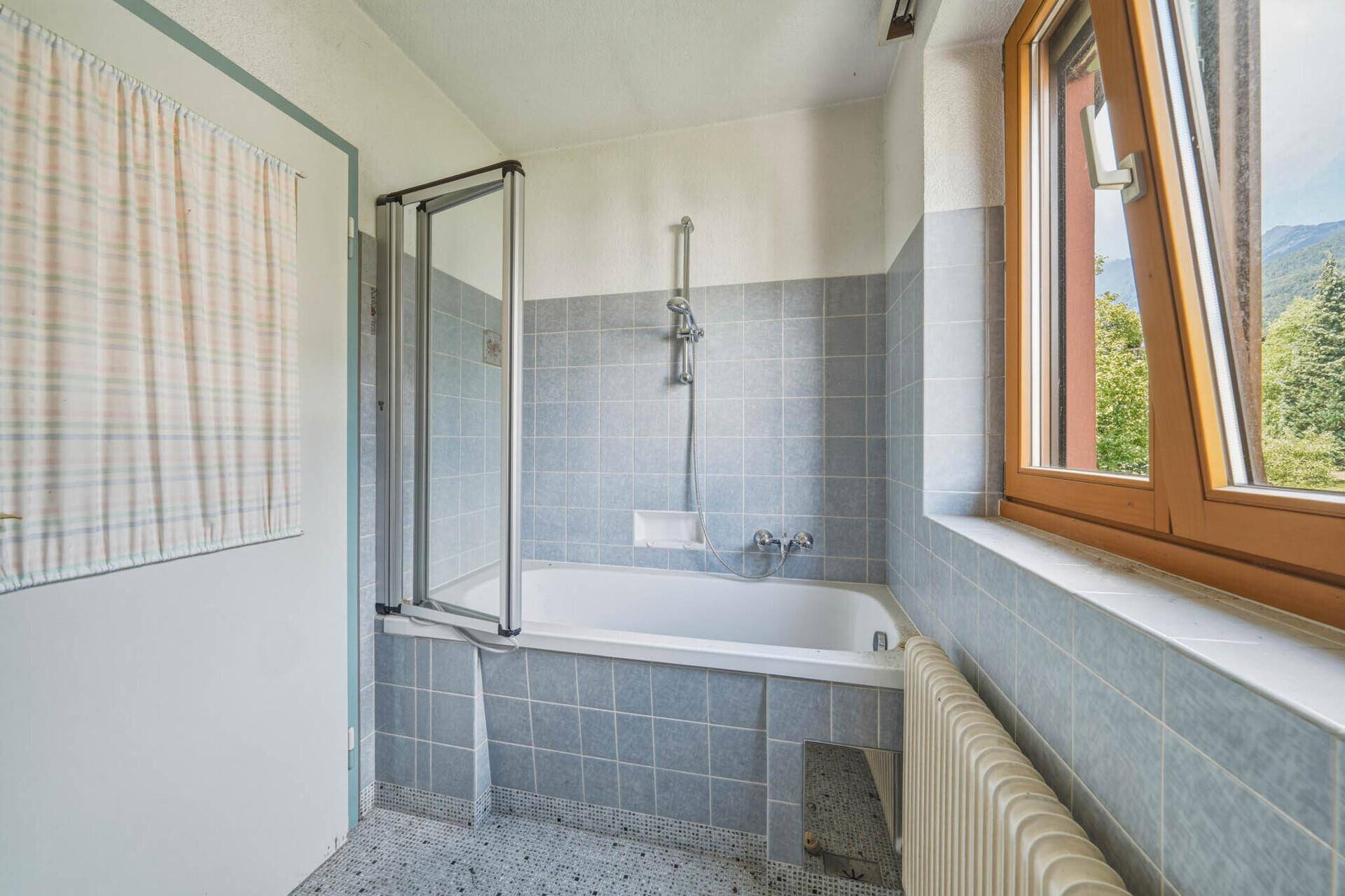 Badezimmer mit blauen Fliesen, Badewanne mit Duschabtrennung und einem Fenster.