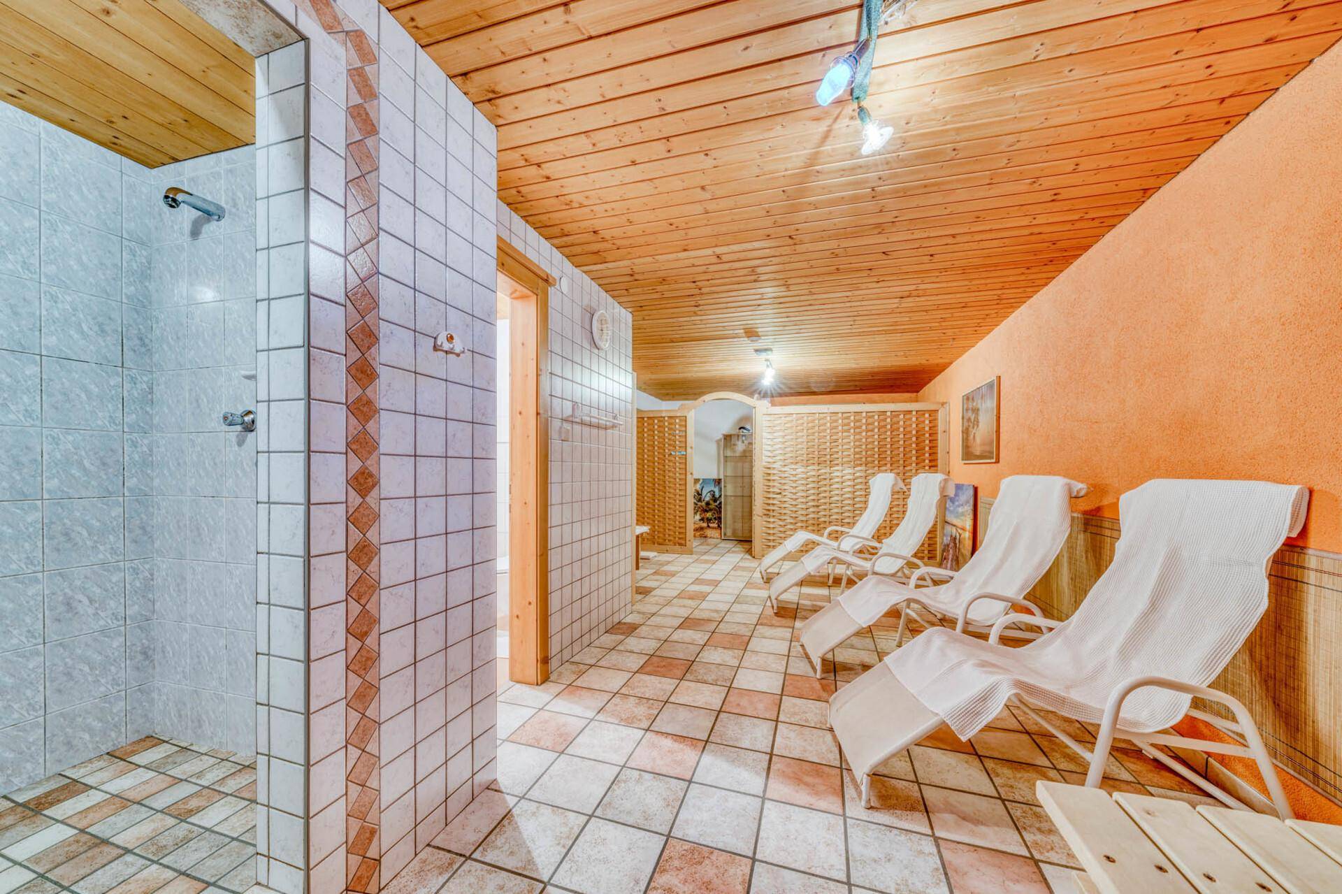 Entspannungsbereich mit Liegestühlen, Holzdecke und integrierter Duschkabine für Erfrischung.