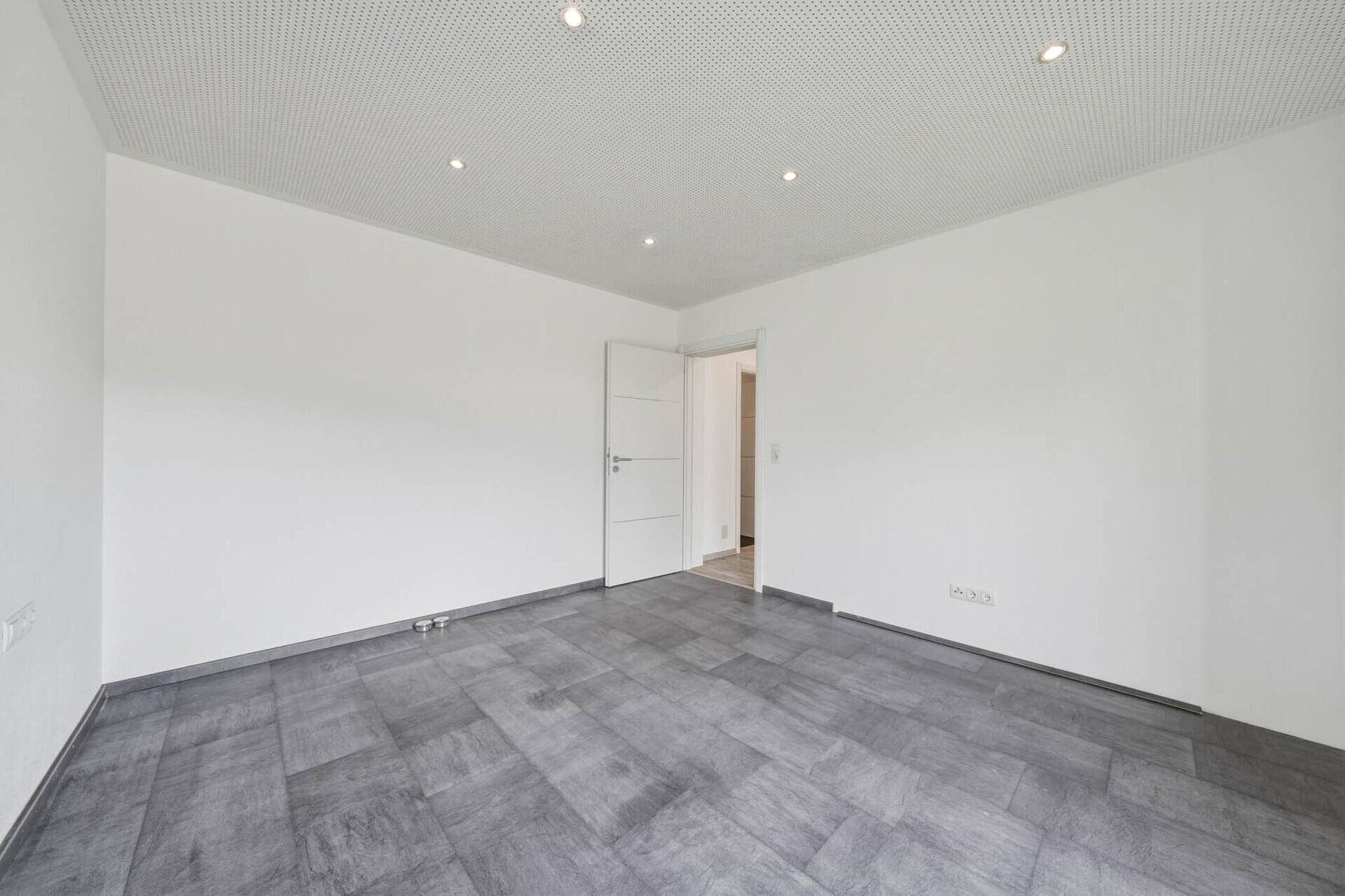 Leeres Zimmer mit modernem grauen Fliesenboden und weißer Decke mit Einbaustrahlern.