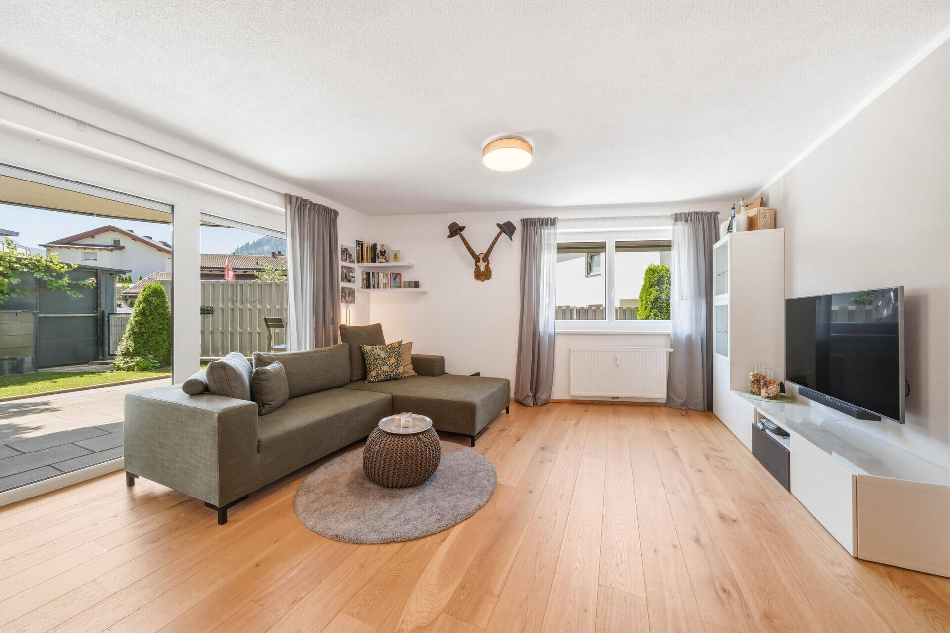 Gemütliches Wohnzimmer mit bequemer Couch, Holzboden und großen Fenstern zum Garten.