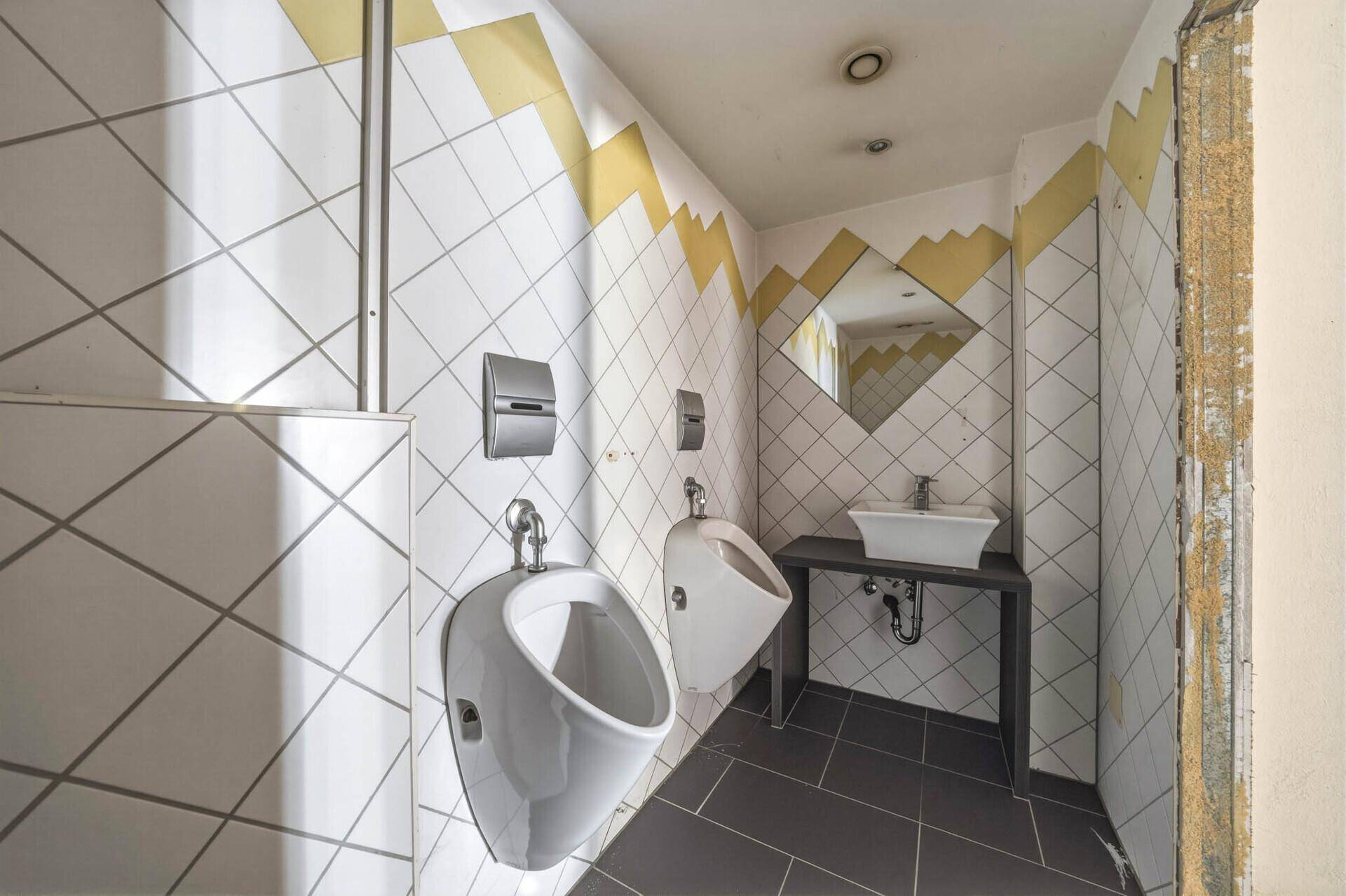 Moderne Gästetoilette mit Urinalen, Waschbecken und diagonalen Fliesen in Weiß und Gelb.