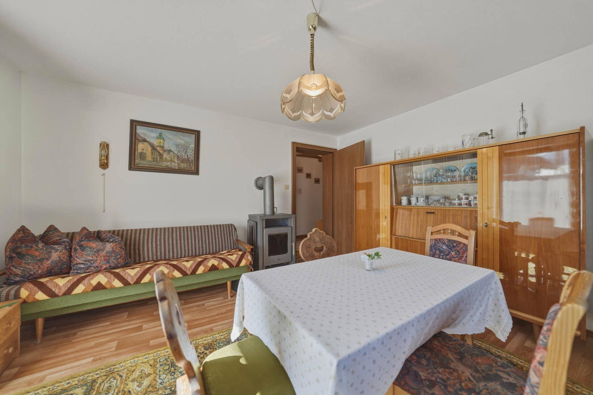 Rustikaler Wohn-Essbereich mit Sofa, Esstisch und einem Kaminofen in traditionellem Ambiente.