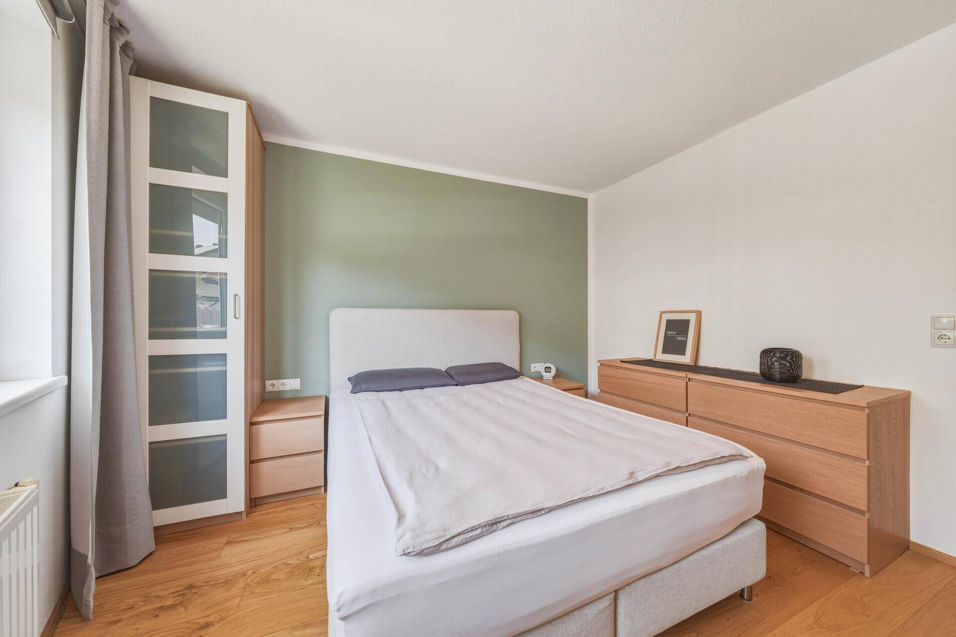 Helles Schlafzimmer mit Holzboden, großem Kleiderschrank und einer grünen Akzentwand.