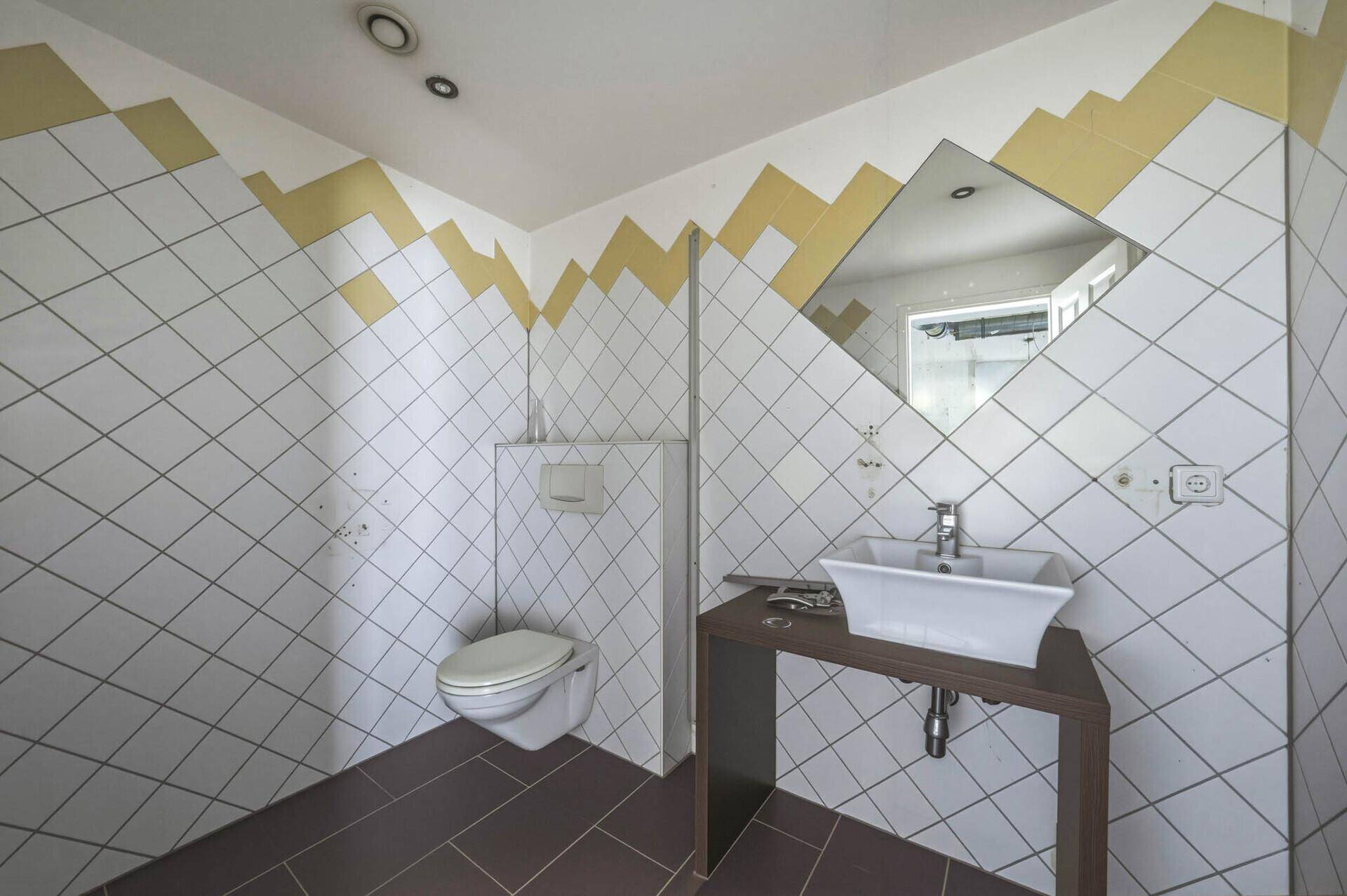 Moderne Gästetoilette mit WC, Waschbecken und diagonalen Fliesen in Weiß und Gelb.