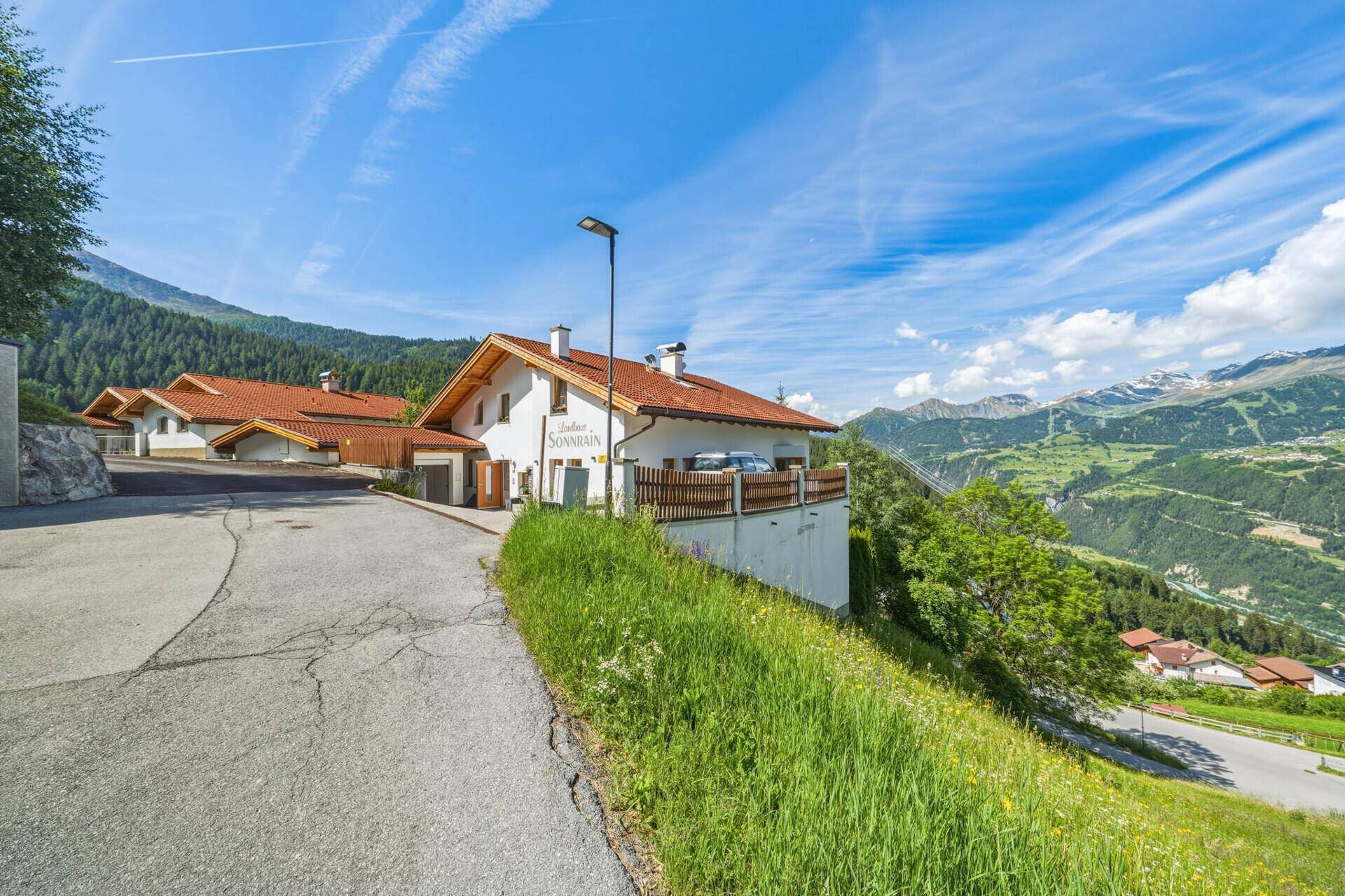 Charmantes Haus an einer Bergstraße mit traditioneller Architektur und weitem Blick auf die Alpen.
