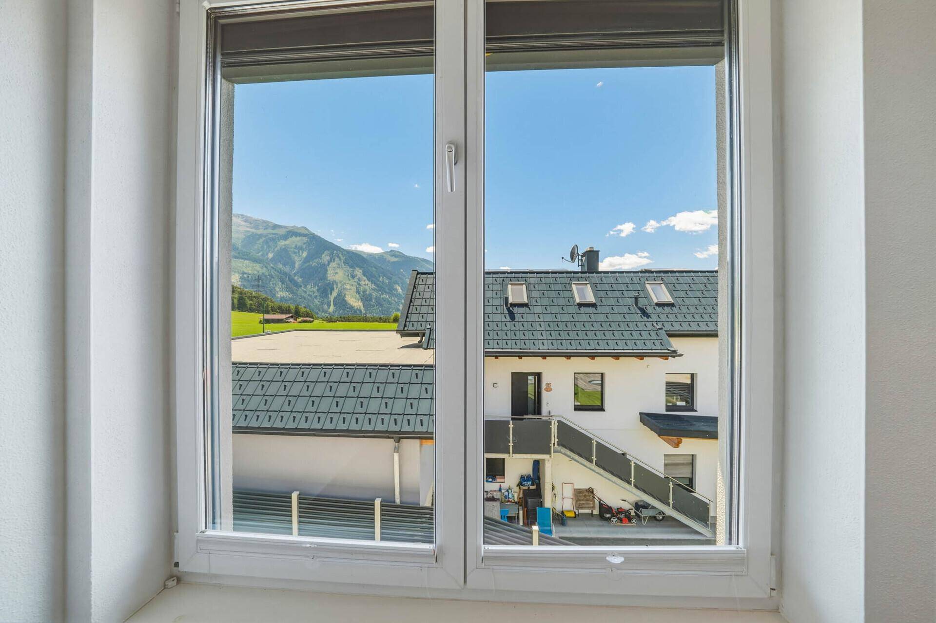 Klarer Ausblick aus dem Fenster auf die Berglandschaft und ein benachbartes Gebäude mit Dachfenstern.