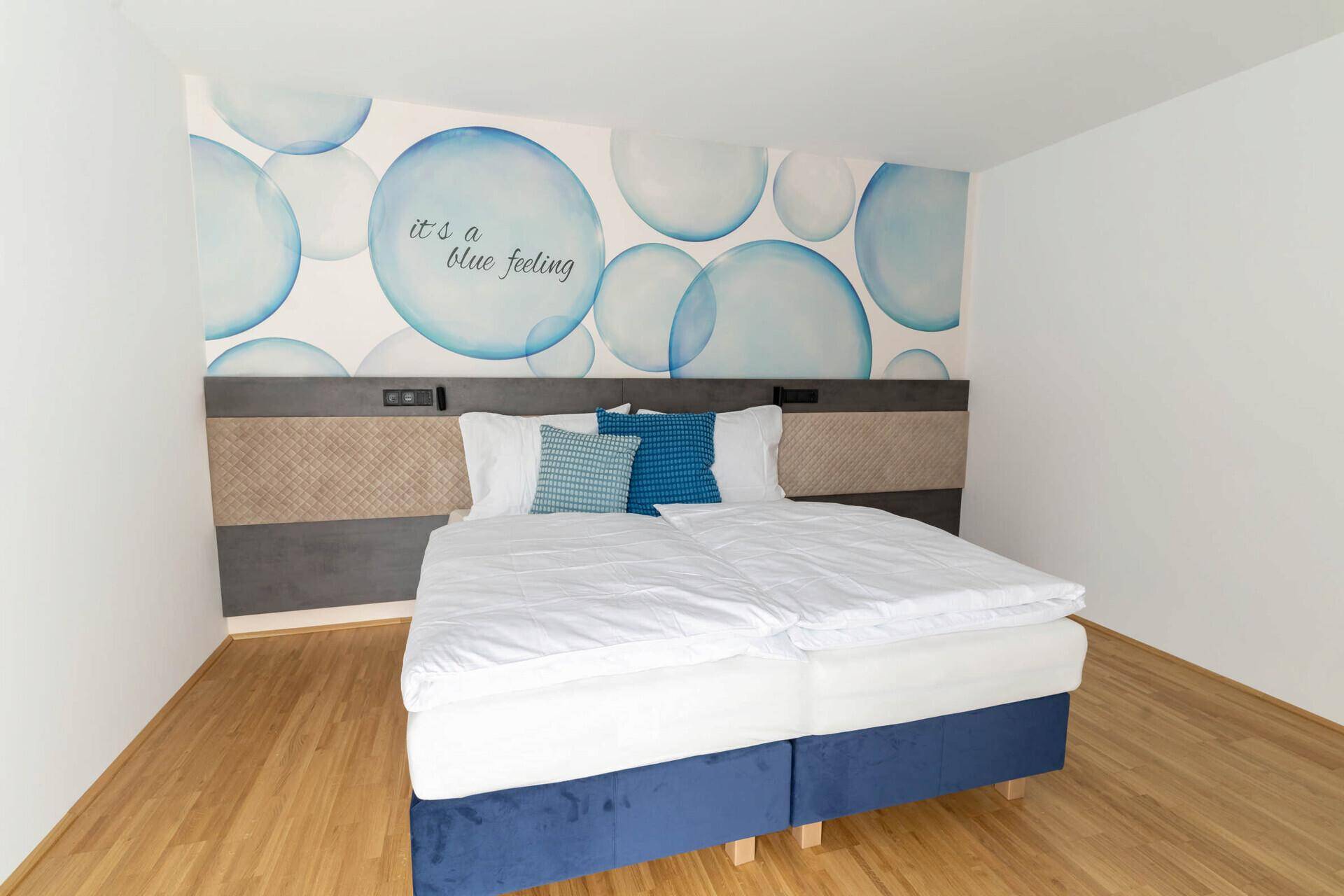 Helles Schlafzimmer mit Doppelbett, Holzboden und Fenster mit Vorhängen.