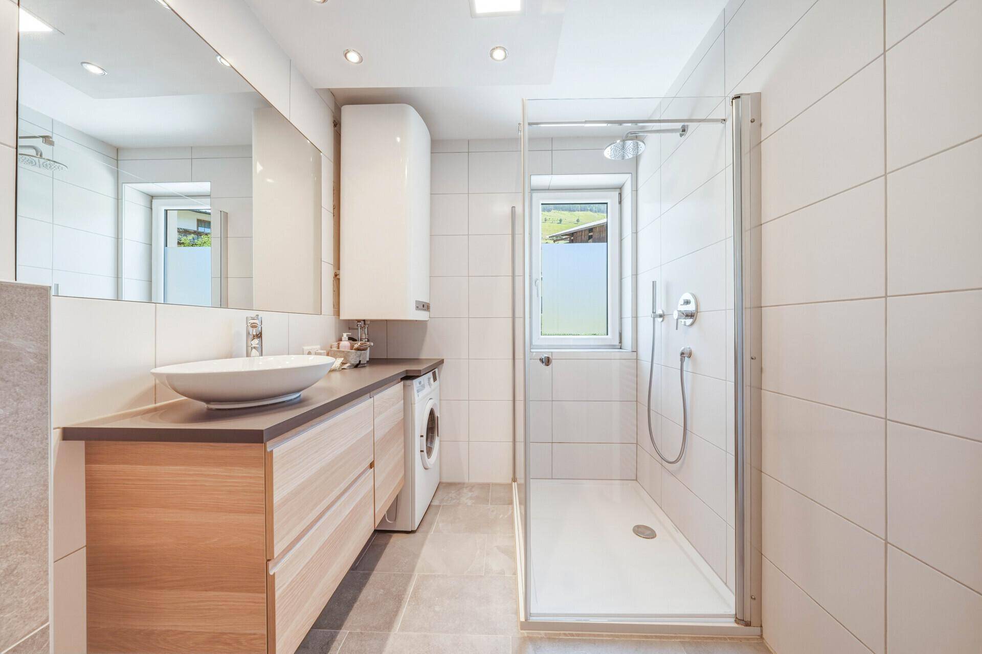 Geräumiges Badezimmer mit großer Dusche, Waschtisch und integrierter Waschmaschine.