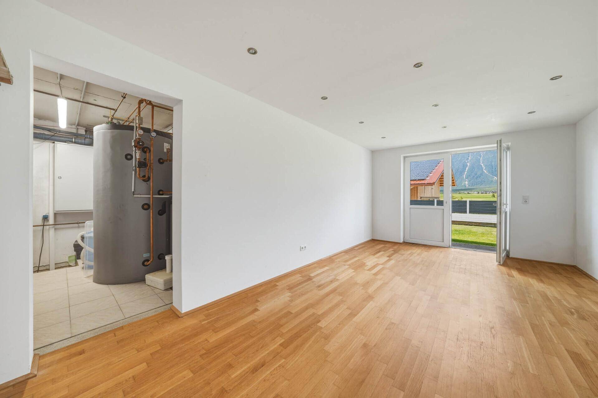 Heller Raum mit Holzboden, weißen Wänden und Zugang zu einem Technikraum sowie Bergblick.