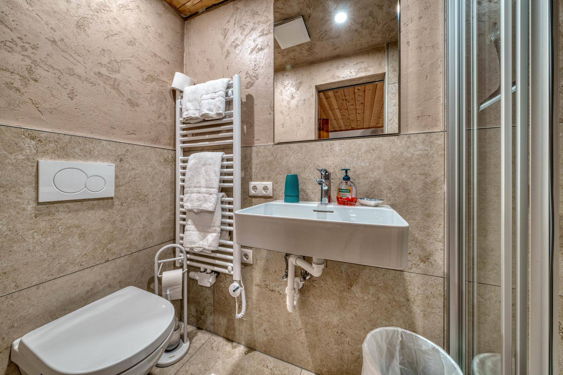 Modernes Badezimmer mit beigefarbenen Fliesen, Wandtoilette, Waschbecken und Duschkabine.