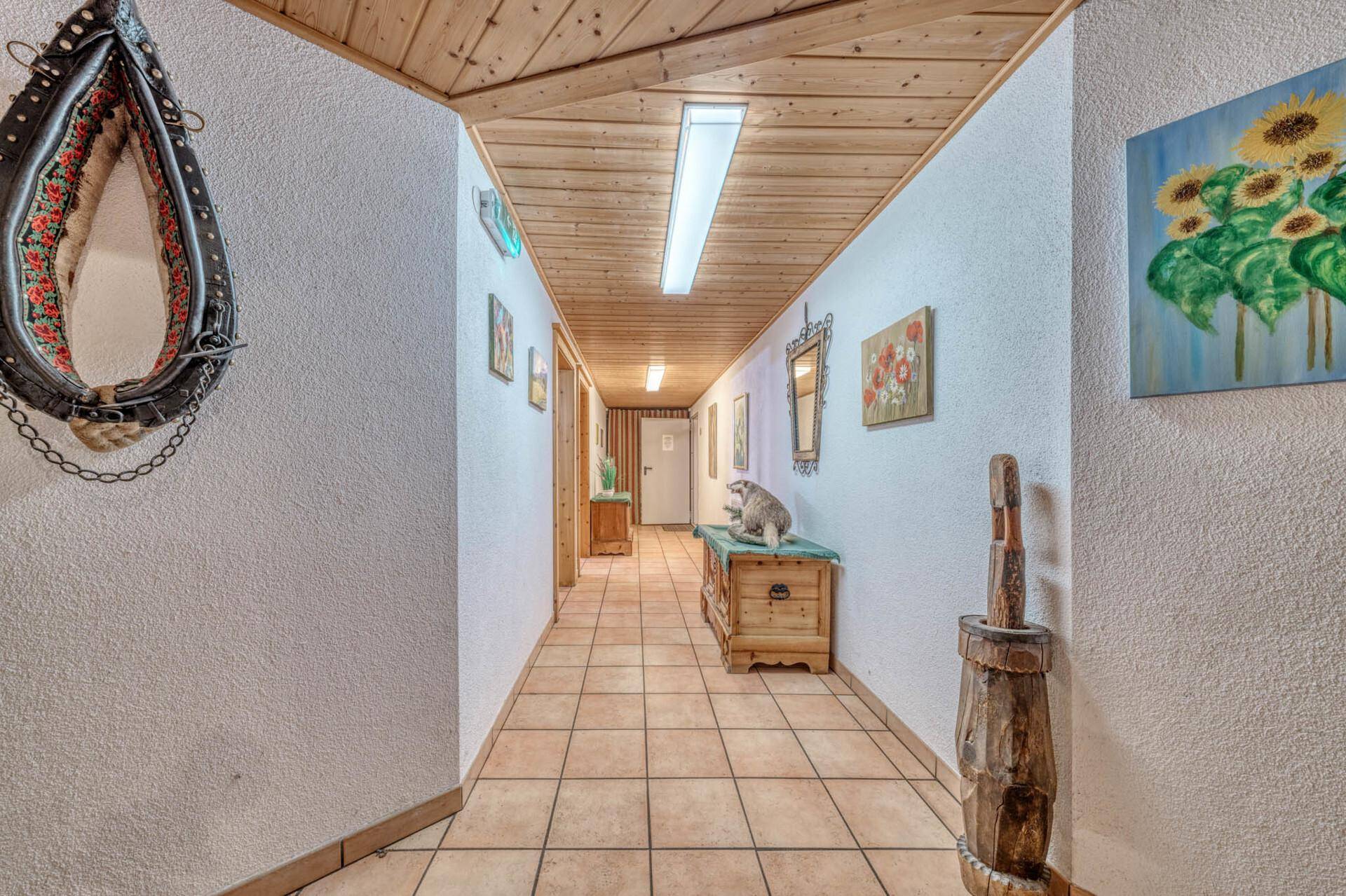 Langer Flur mit Fliesenboden, Holzdecke und traditionellen Möbeln und Bildern.