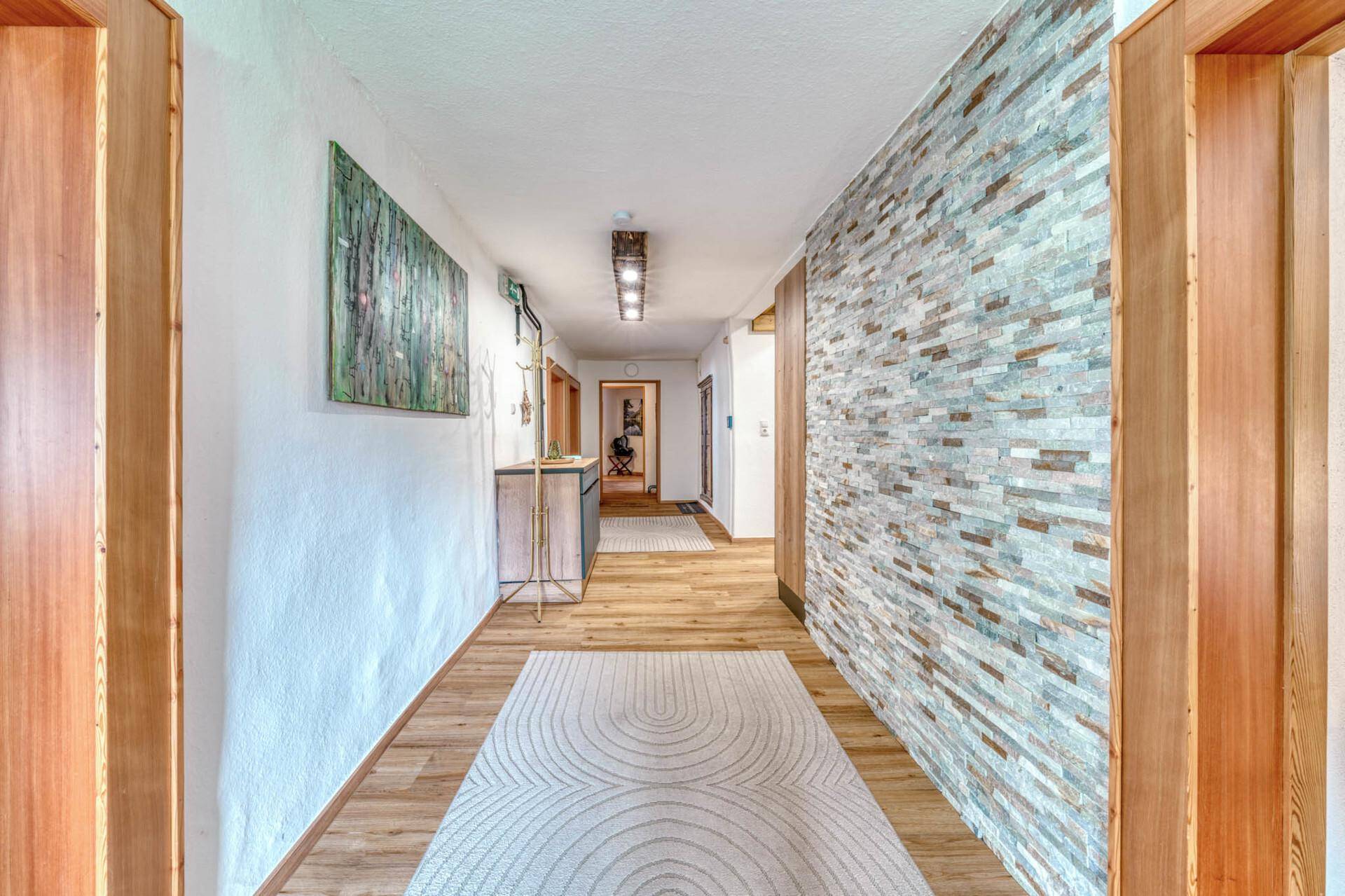 Langer Flur mit Holzboden, Steinwandakzent und moderner Beleuchtung, einladend gestaltet.