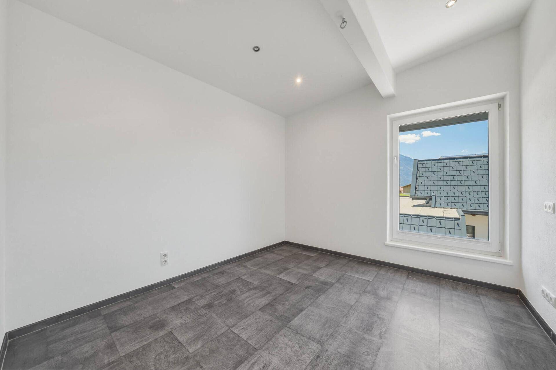 Helles Zimmer mit modernen Fliesen und einem Fenster mit Blick auf ein angrenzendes Gebäude.