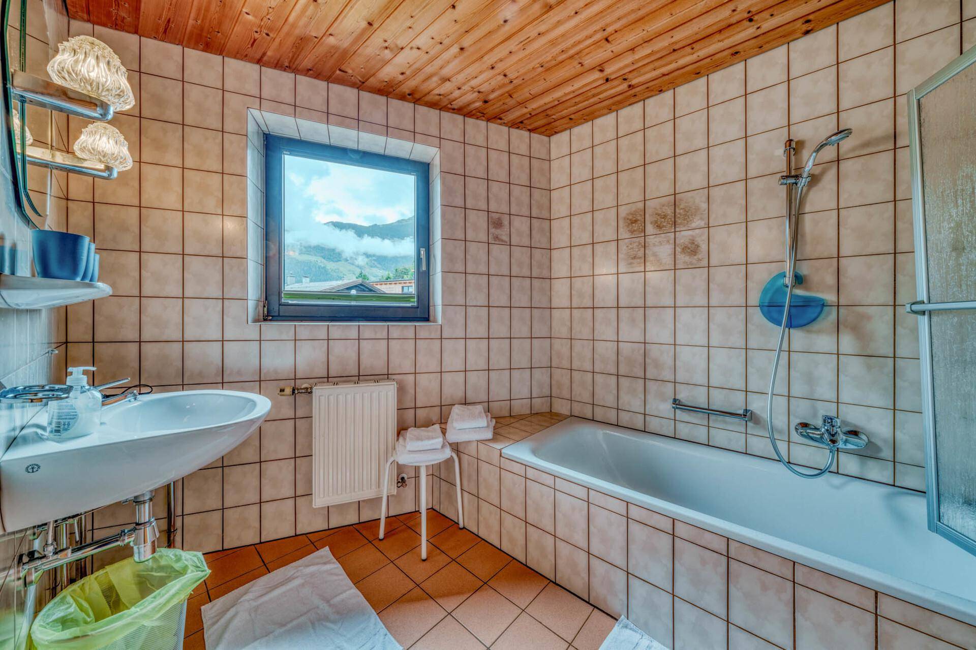 Gefliestes Badezimmer mit Badewanne, Dusche und Fenster mit Bergblick.