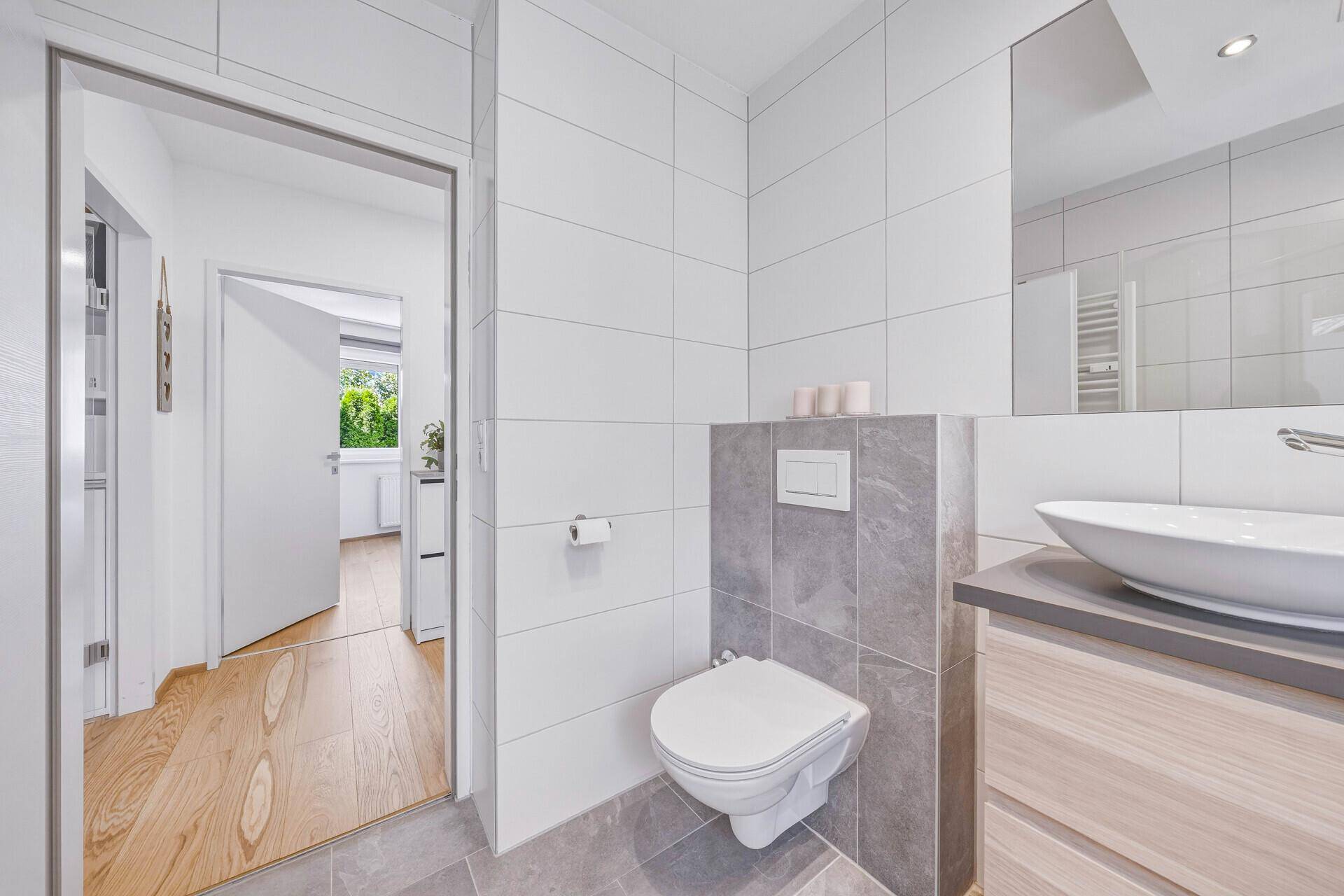 Modernes Badezimmer mit Wand-WC und Waschtisch, mit Blick in den angrenzenden Flur.