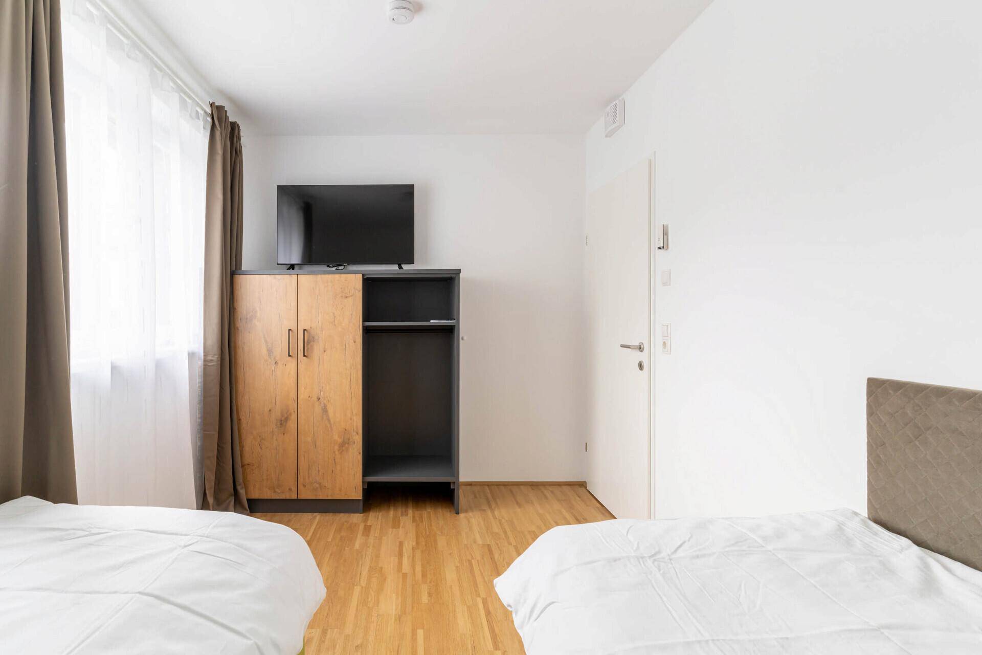 Schlafzimmer mit zwei Einzelbetten, Holzboden und einem Kleiderschrank mit Fernseher.