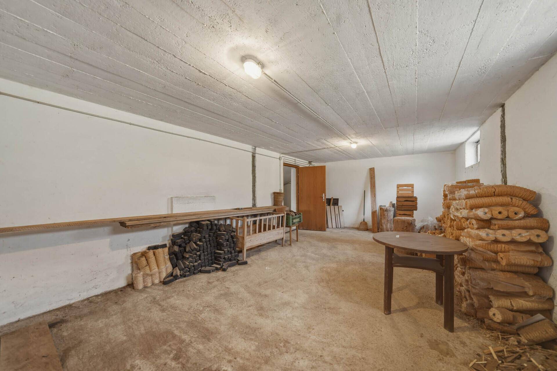 Geräumiger Kellerraum mit Betonboden, Holzstapeln und einfacher Beleuchtung.