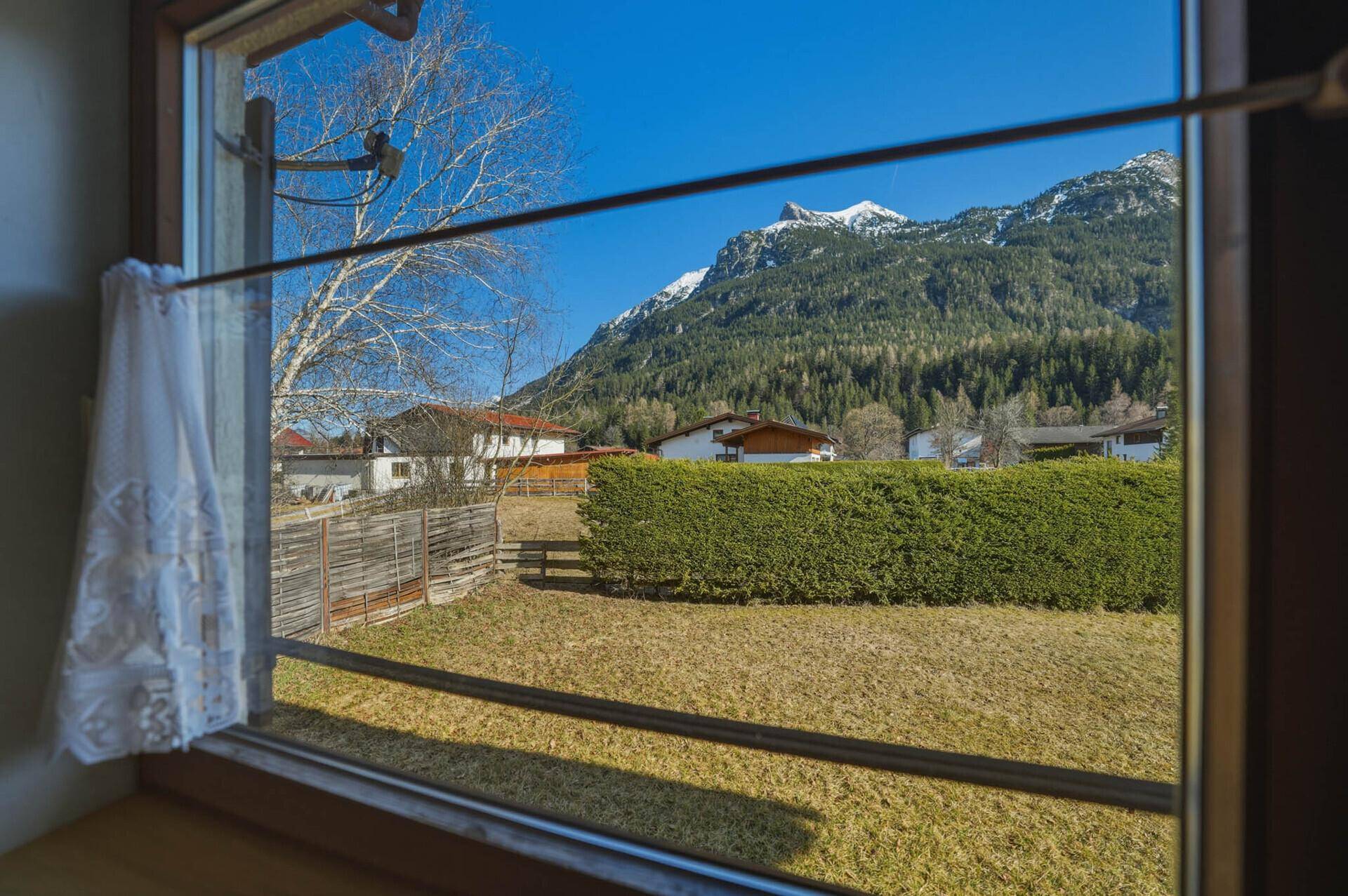 Fensterblick auf die umliegende Berglandschaft und einen gepflegten Gartenbereich.