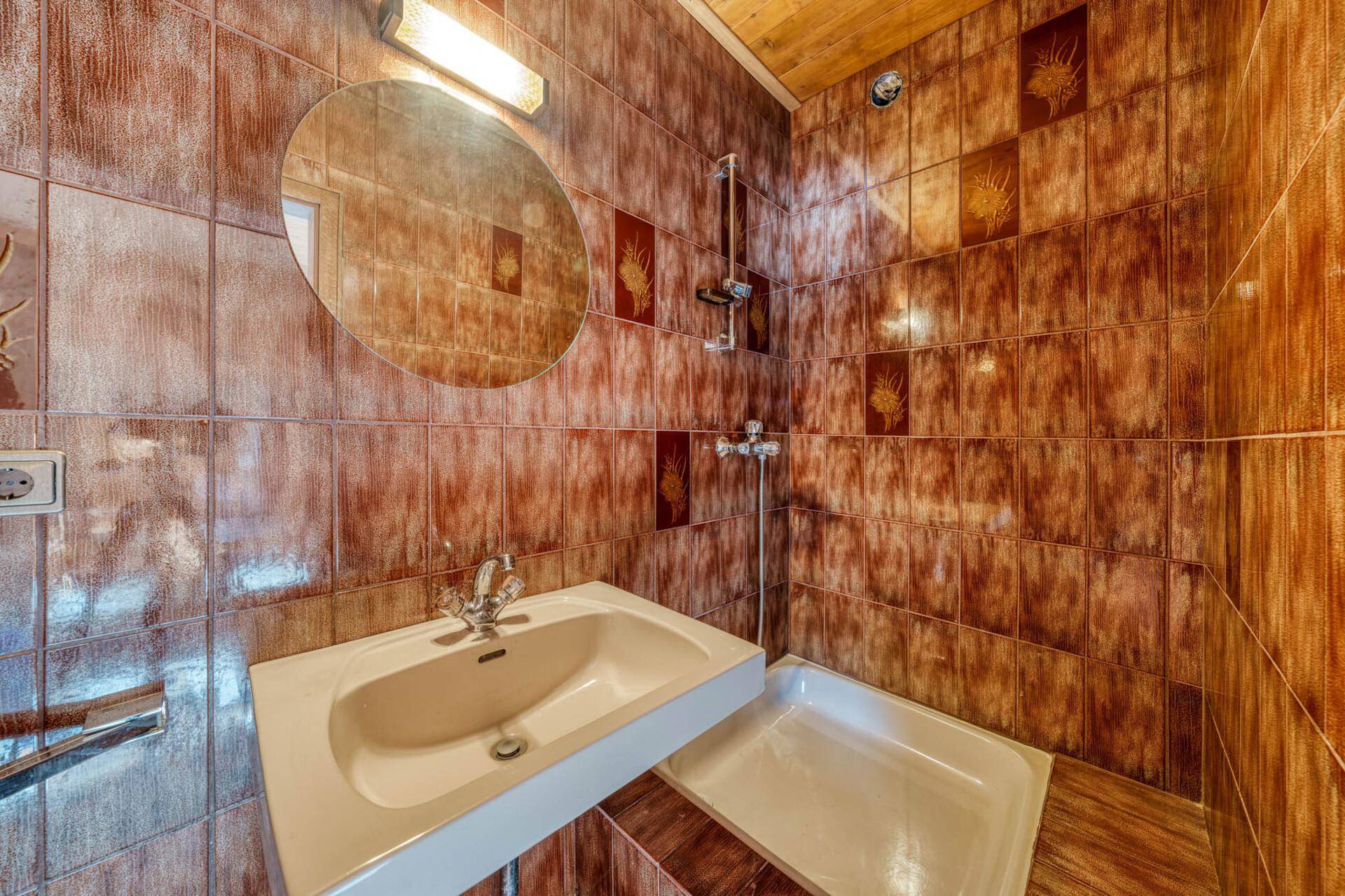 Badezimmer im 80er-Jahre-Stil mit braunen Fliesen, Dusche und Holzdecke.