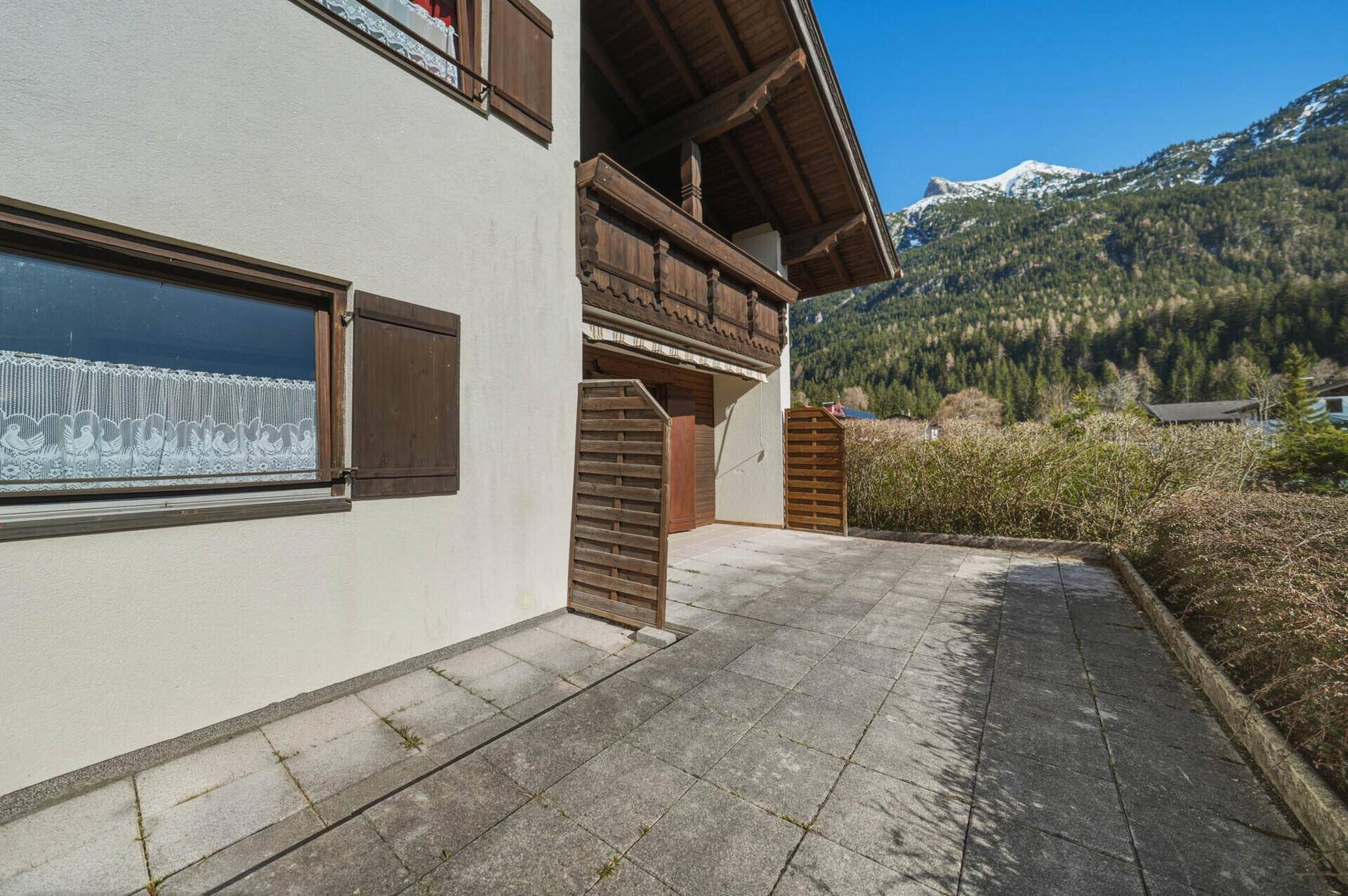 Gepflasterte Terrasse neben dem Haus mit Bergblick und traditionellem Balkon.