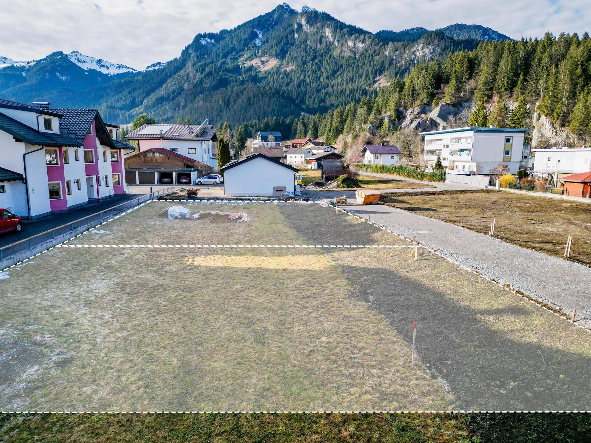 Baugrundstück in ländlicher Umgebung mit angrenzenden Häusern und einem schönen Blick auf die Berge.