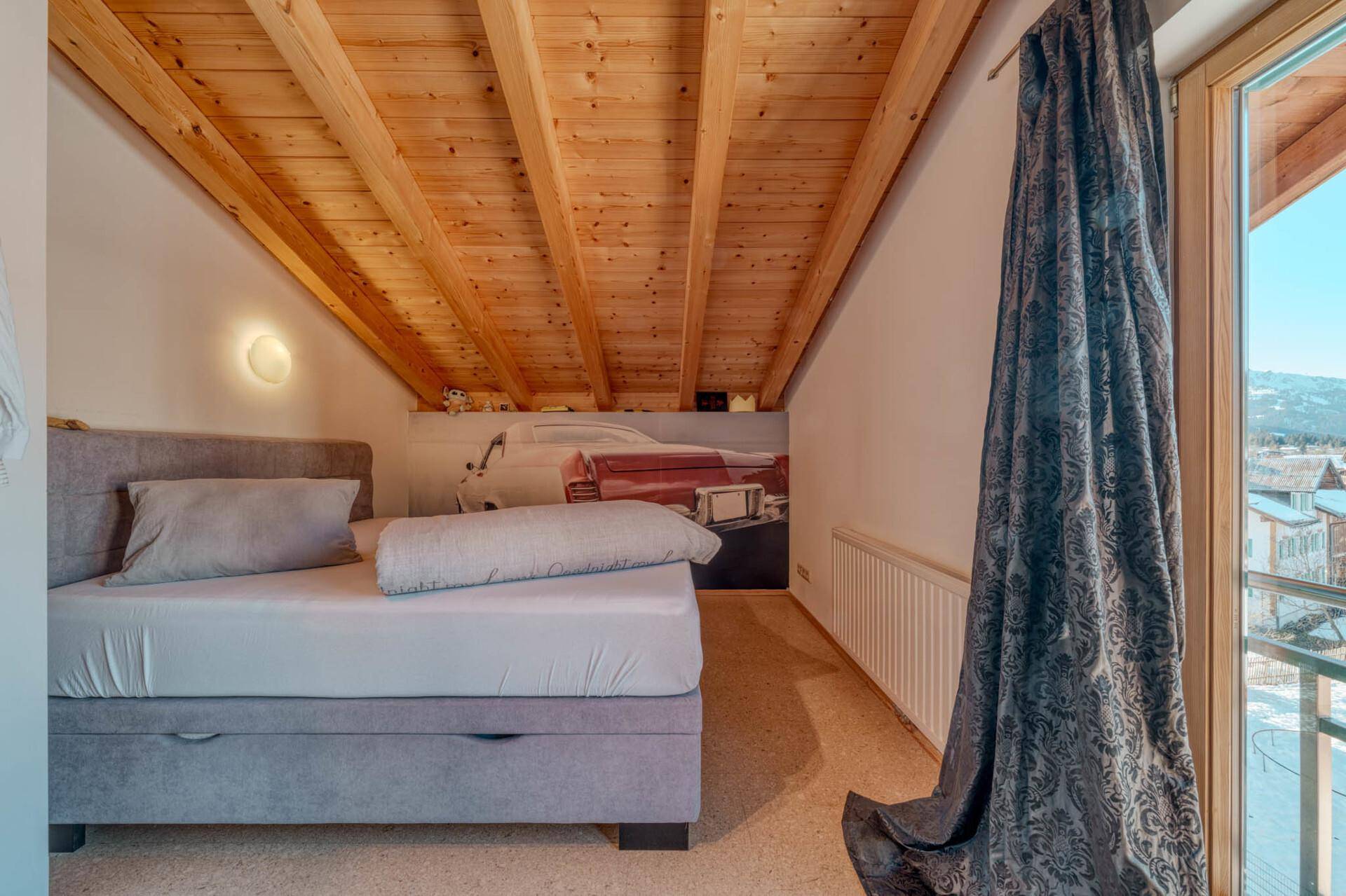 Gemütliches Schlafzimmer im Dachgeschoss mit Holzbalkendecke und Einzelbett.