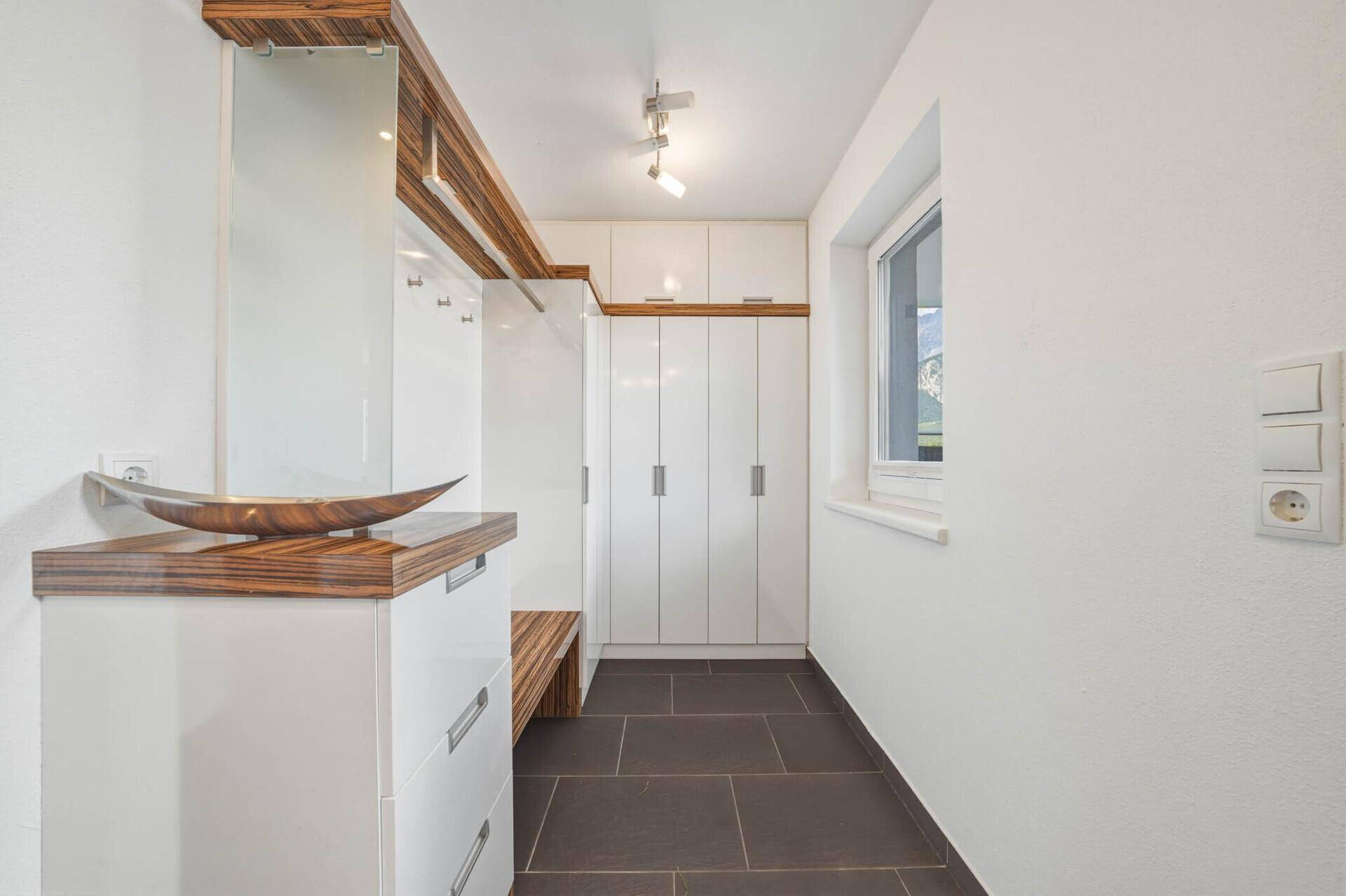 Heller Flur mit Einbauschränken, Spiegel und Fenster, ideal für Garderobe und Stauraum.