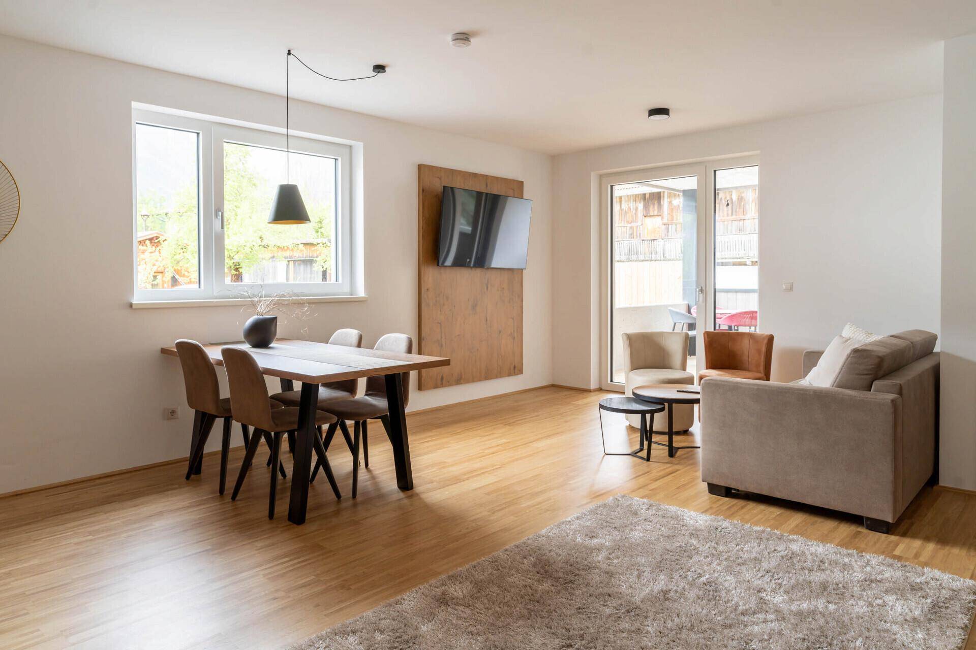 Heller Wohn-Essbereich mit Holzboden, Esstisch und Zugang zum Balkon.