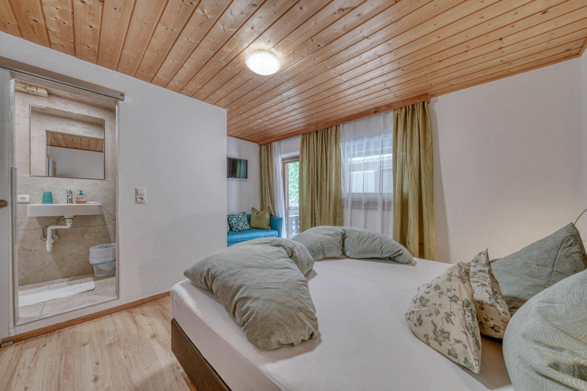 Gemütliches Schlafzimmer mit Holzbalkendecke, Doppelbett und integriertem Waschbereich.