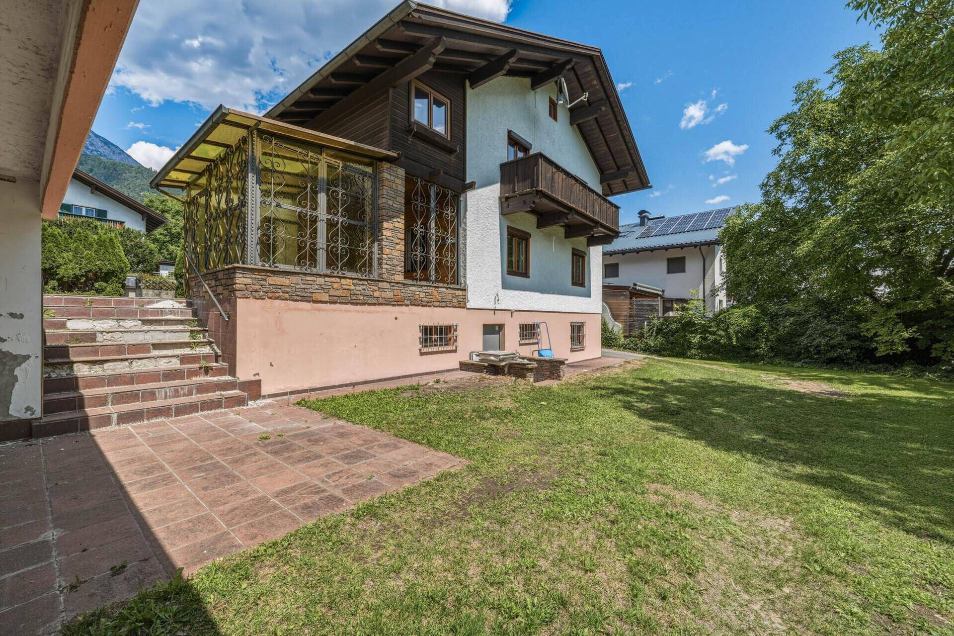 Seitenansicht des Hauses mit Wintergarten, gepflasterter Terrasse und weitläufigem Rasen.