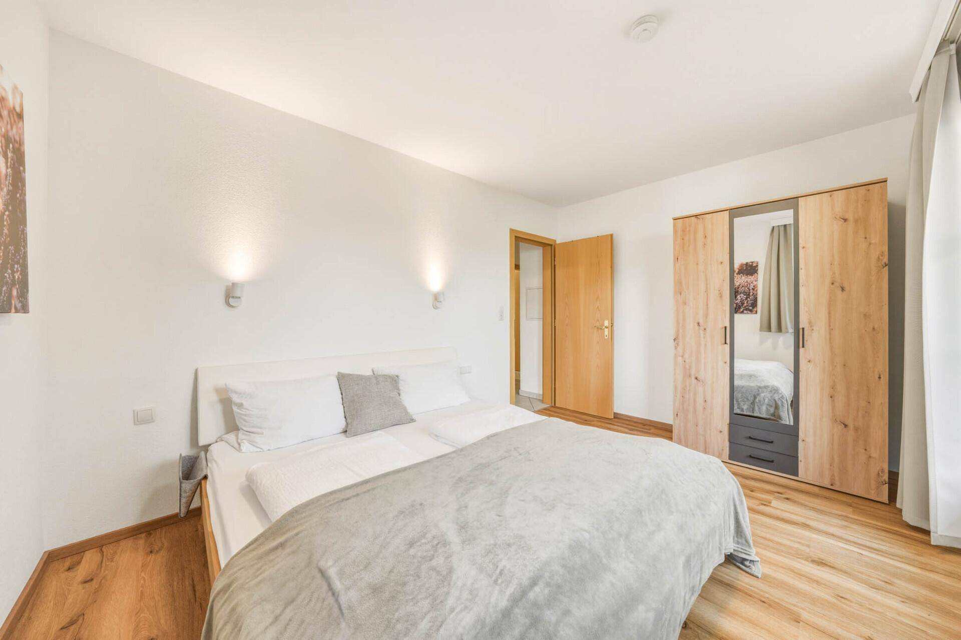 Schlafzimmer mit Doppelbett, Holzboden und einem geräumigen Holzschrank mit Spiegeltür.