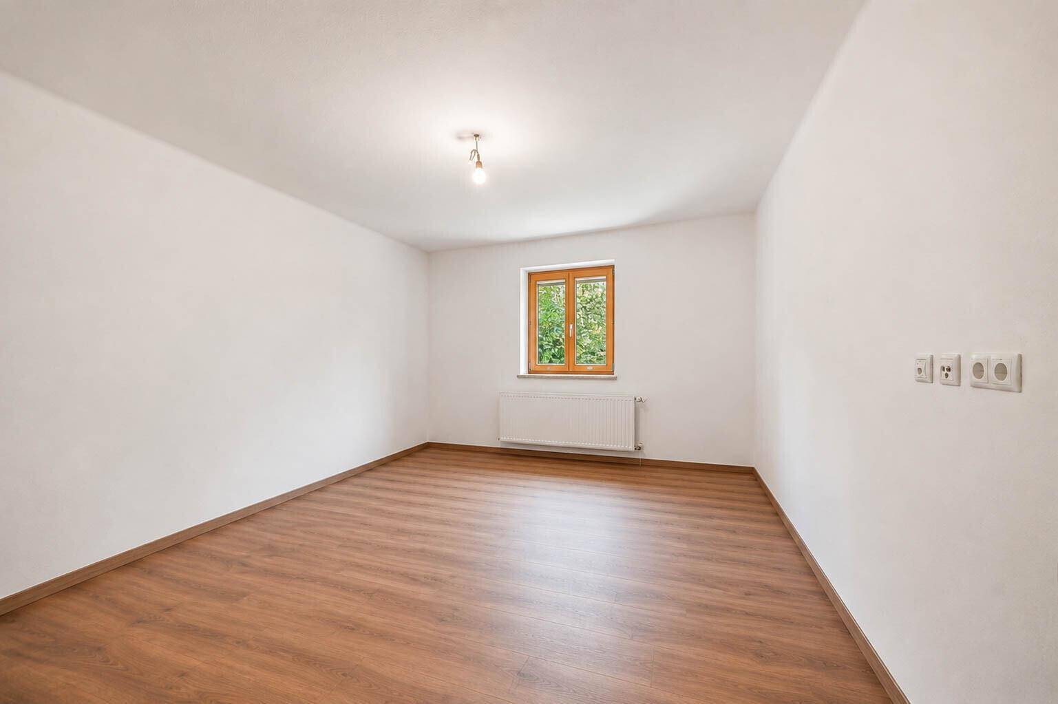 Helles, unmöbliertes Zimmer mit Laminatboden, weiß gestrichenen Wänden und einem Fenster.