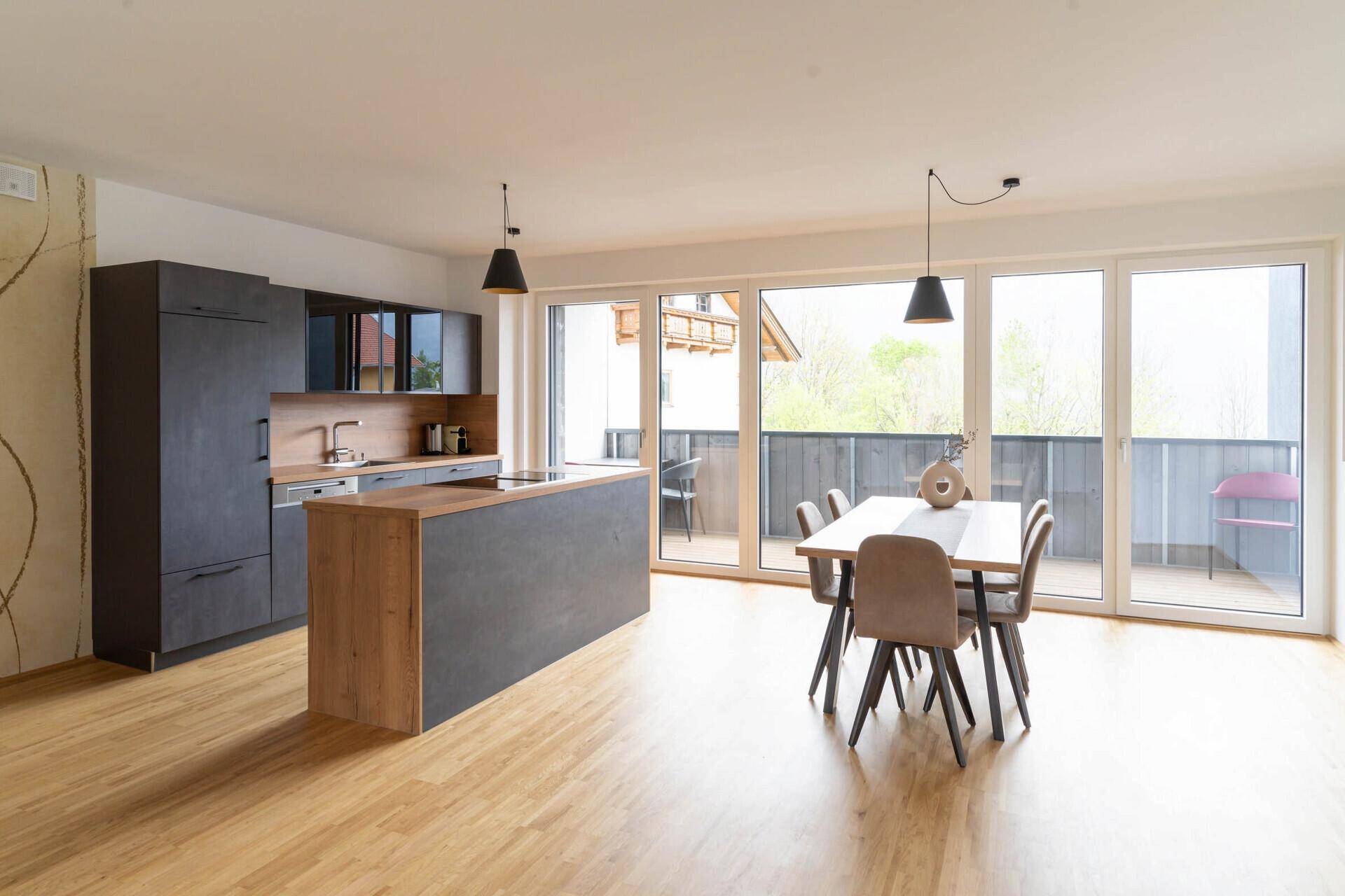 Offener Wohn-Essbereich mit moderner Küche, Holzboden und Zugang zum Balkon.