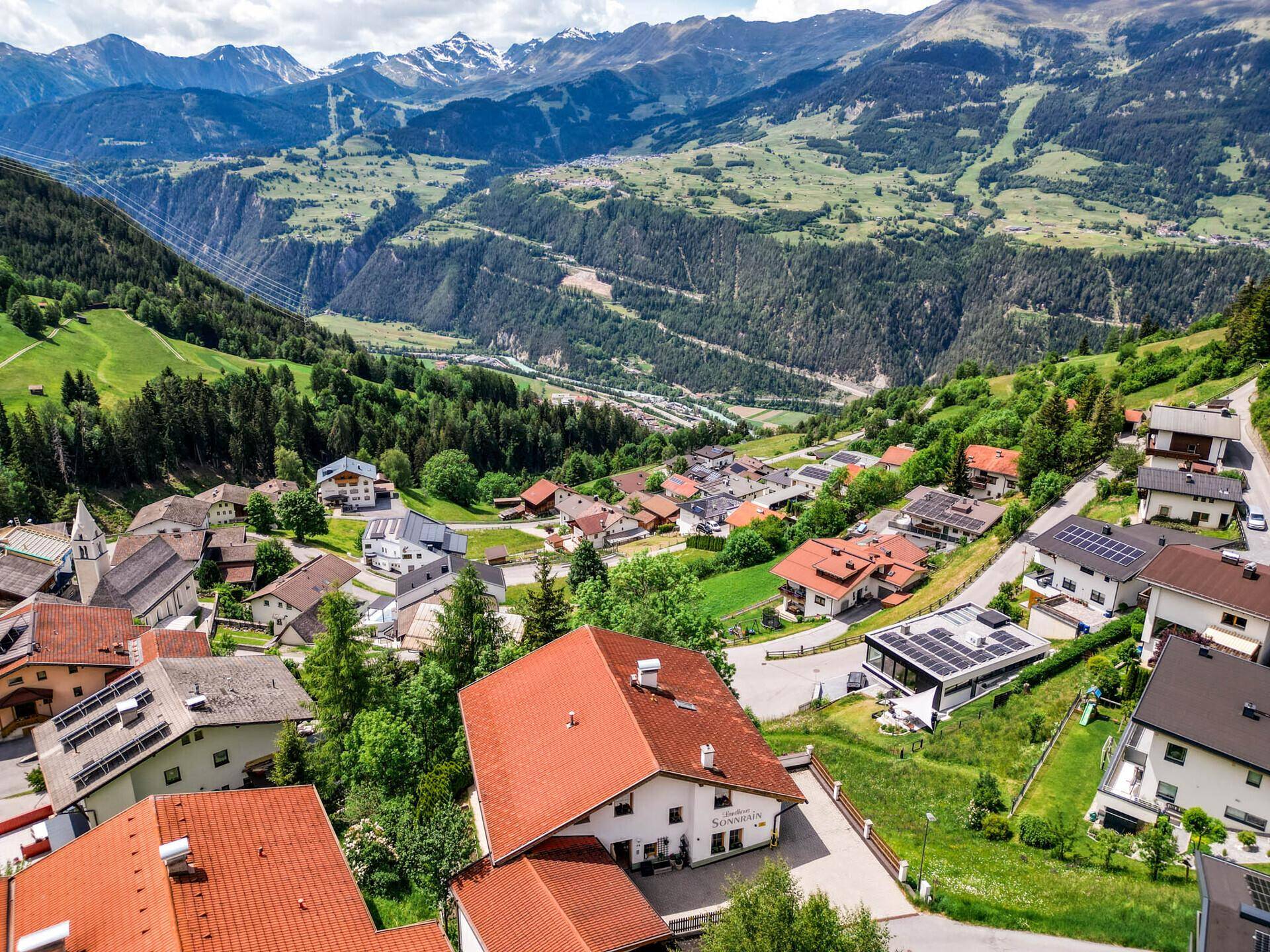 Luftaufnahme des Anwesens und umliegender Häuser am Hang mit Blick auf das Tal und die Berge.