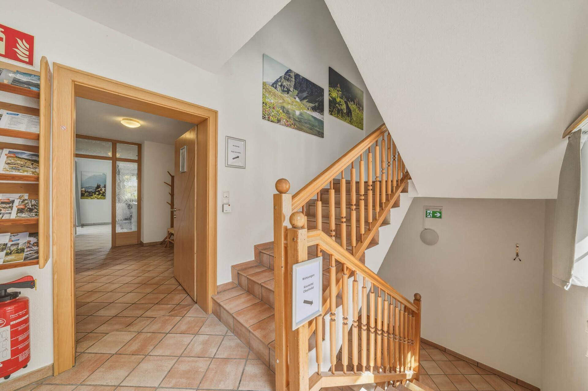 Holztreppe mit Geländer und gefliesten Stufen, die zu den oberen Etagen führt.