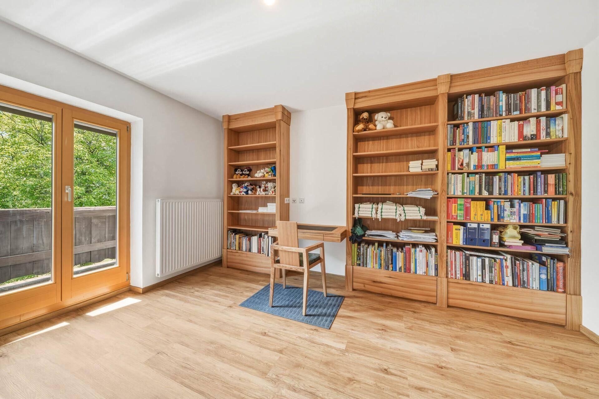 Arbeitszimmer mit Holzbücherregalen, Schreibtisch und Balkonzugang, hell und funktional.