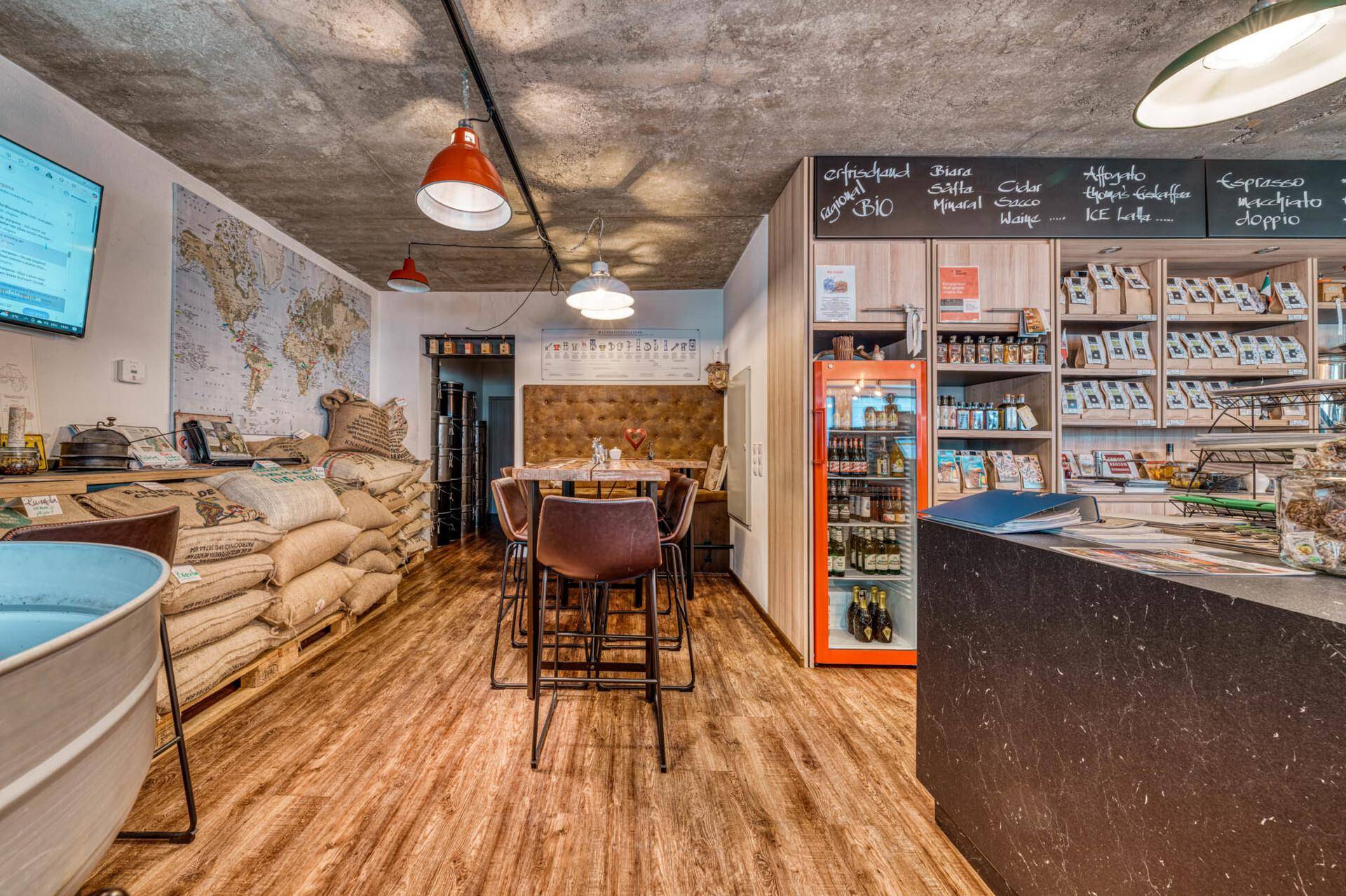 Gemütlicher Sitzbereich in einem Hofladen mit Holztisch, Barhockern und Weltkarte an der Wand.