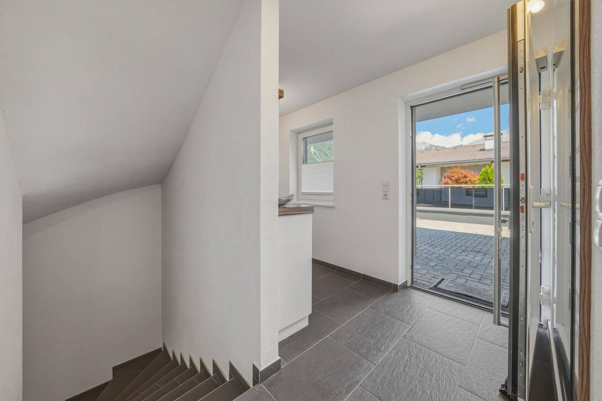 Eingangsbereich mit gefliestem Boden, Treppe und einer modernen Glastür zum Außenbereich.
