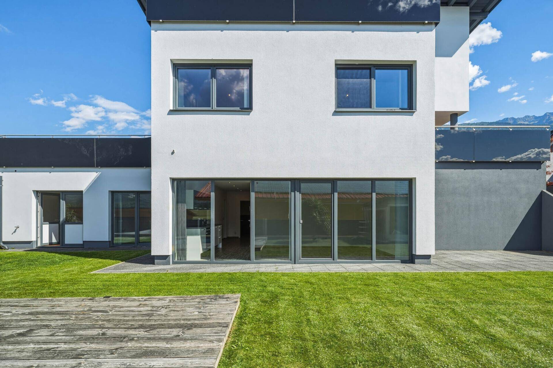 Rückfassade des Hauses mit großen Glasfronten, die zum Garten und Holzdeck führen.
